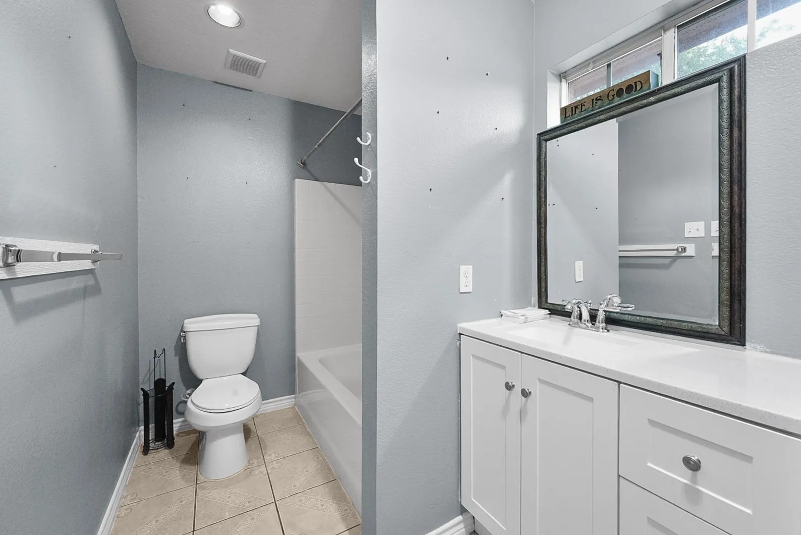 White shaker-style vanity with a single basin sink, silver-finish faucet, and a large framed mirror