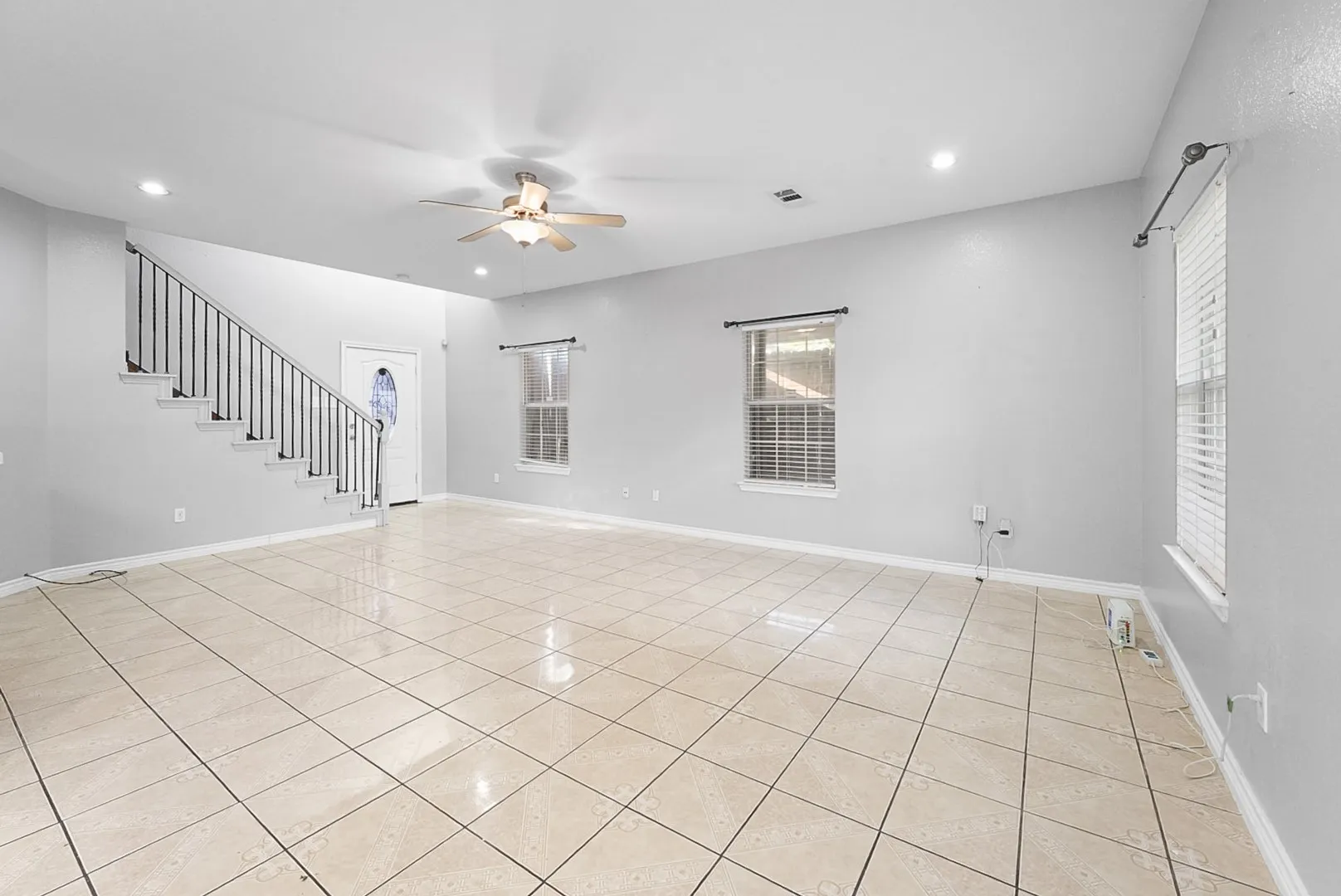 Spacious room featuring tile flooring, a staircase with metal balusters, recessed lighting, and a ceiling fan