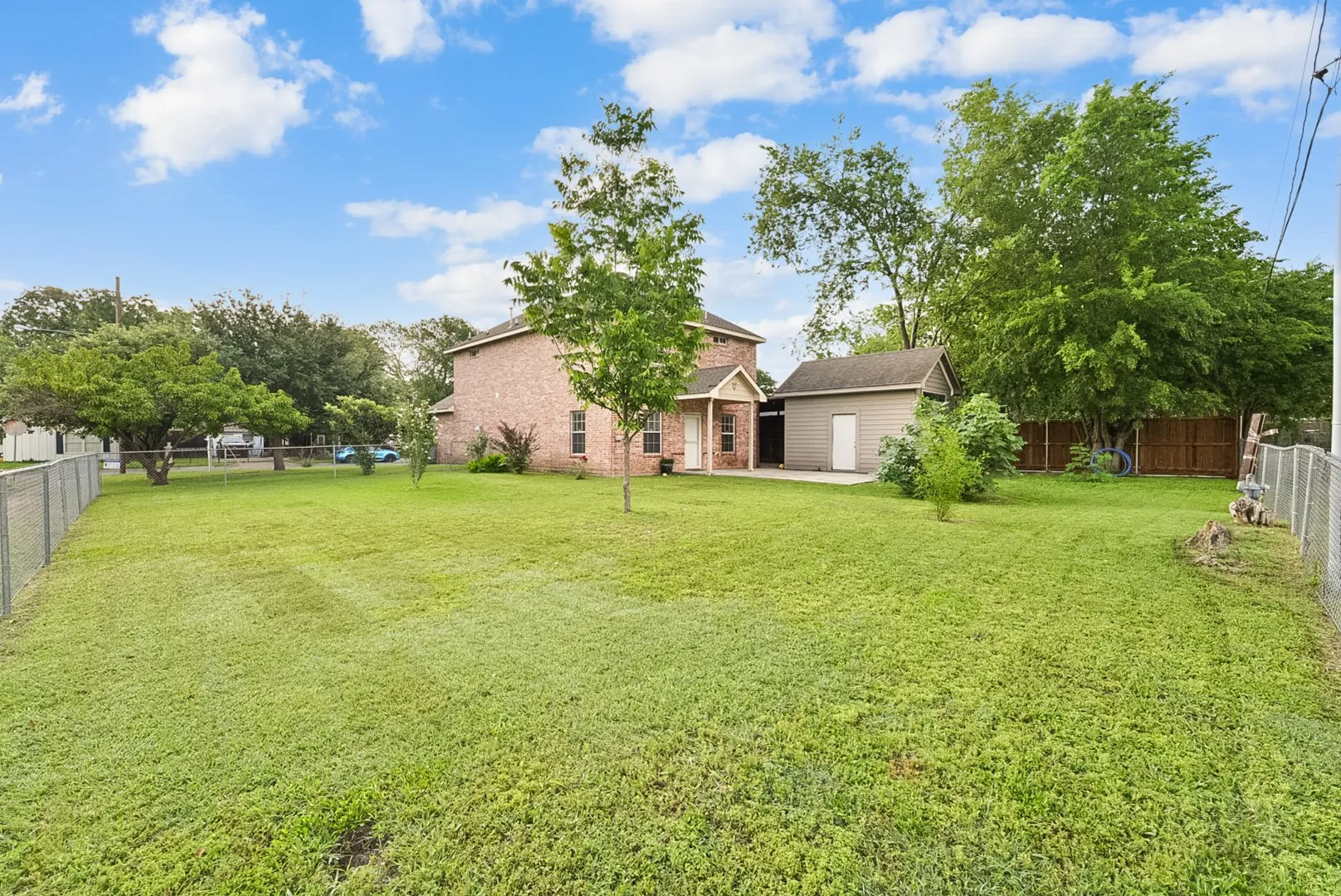 Expansive grassy yard with mature trees, a detached storage shed, and chain-link fencing