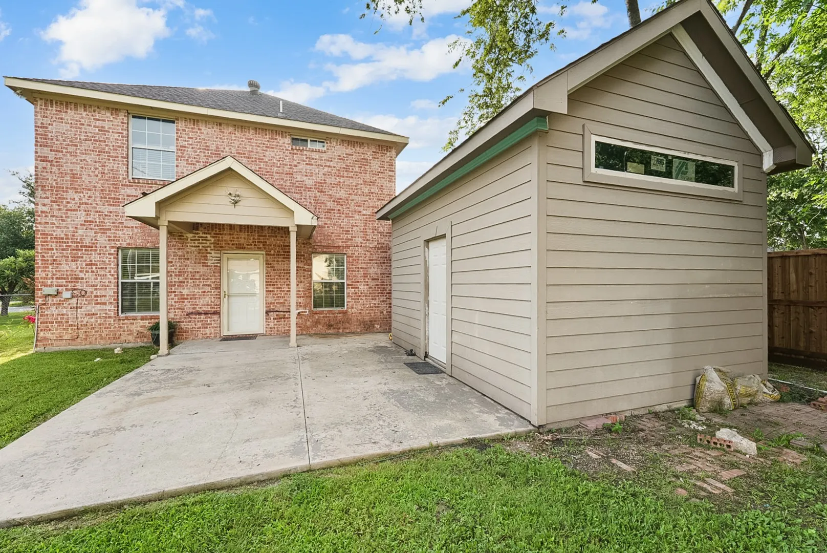 Brick exterior with a covered entryway, concrete patio, and separate siding-clad structure with a rectangular window