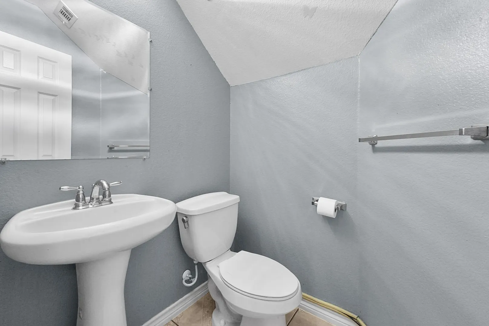 Pedestal sink with chrome fixtures and a wall-mounted mirror