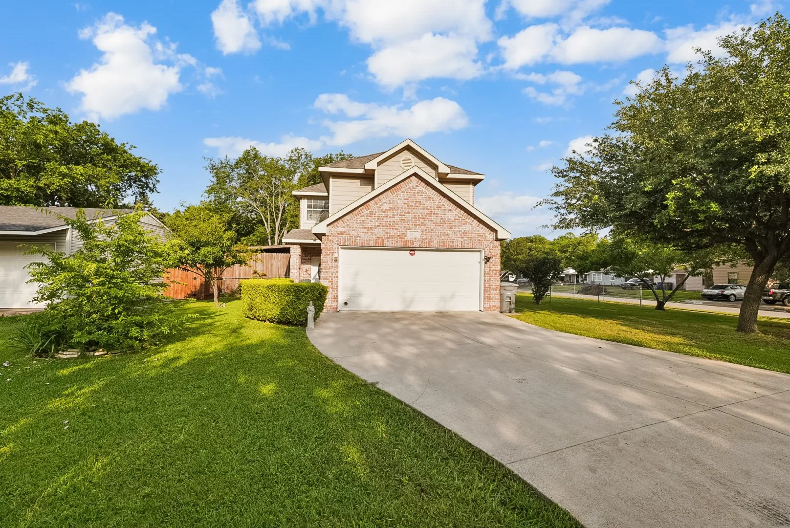 Brick and siding exterior, two-car garage, concrete driveway, front lawn, and mature trees