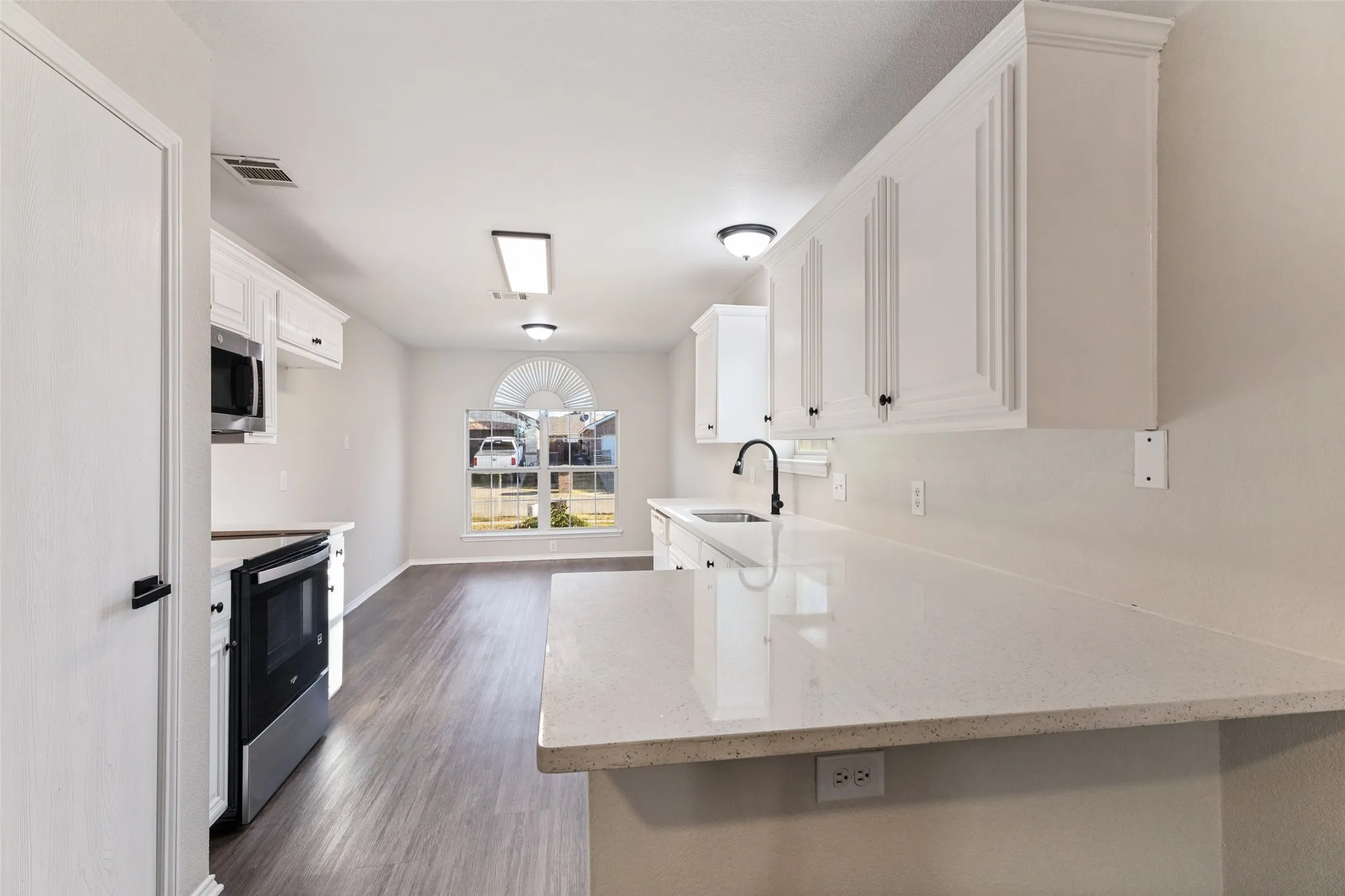 White cabinetry with black hardware, light-toned countertops, wood-finish flooring, stainless steel appliances, and a rounded arch window