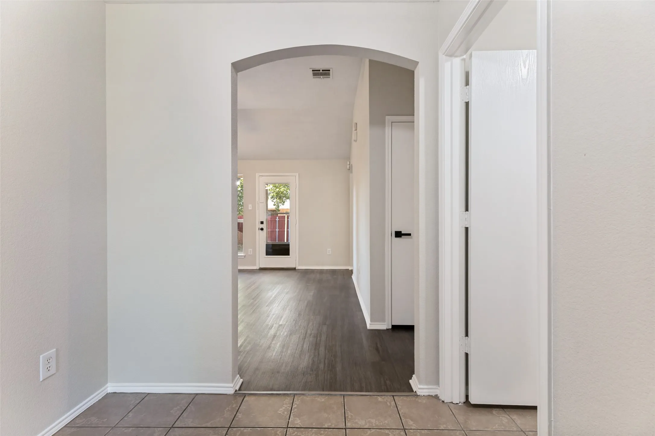 Archway entry to interior space, featuring tile flooring transitioning to wood-finish flooring, and a white door with matte black hardware