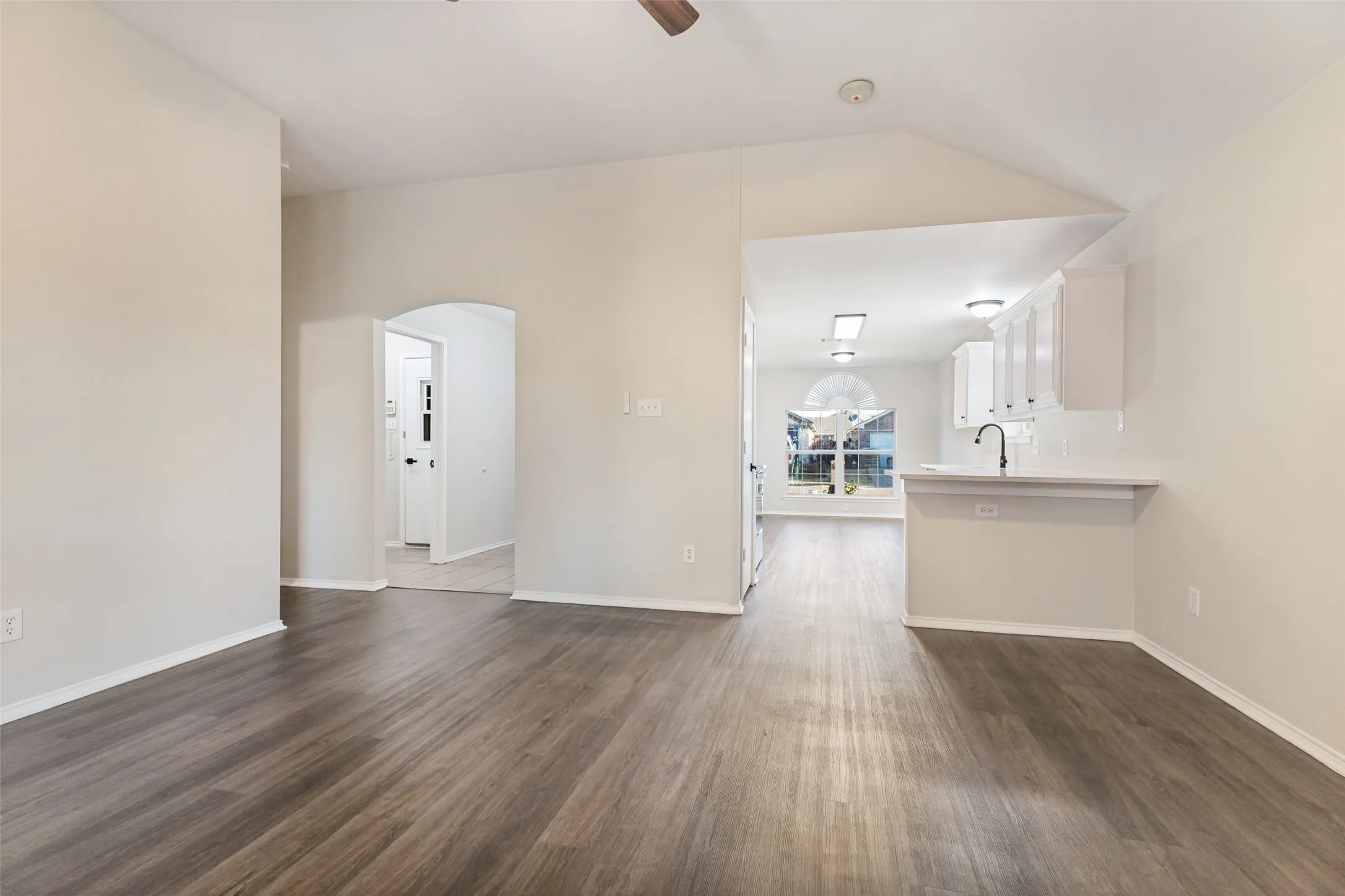 Vaulted ceiling, wood-finish flooring, arched doorway, kitchen pass-through, and a ceiling fan