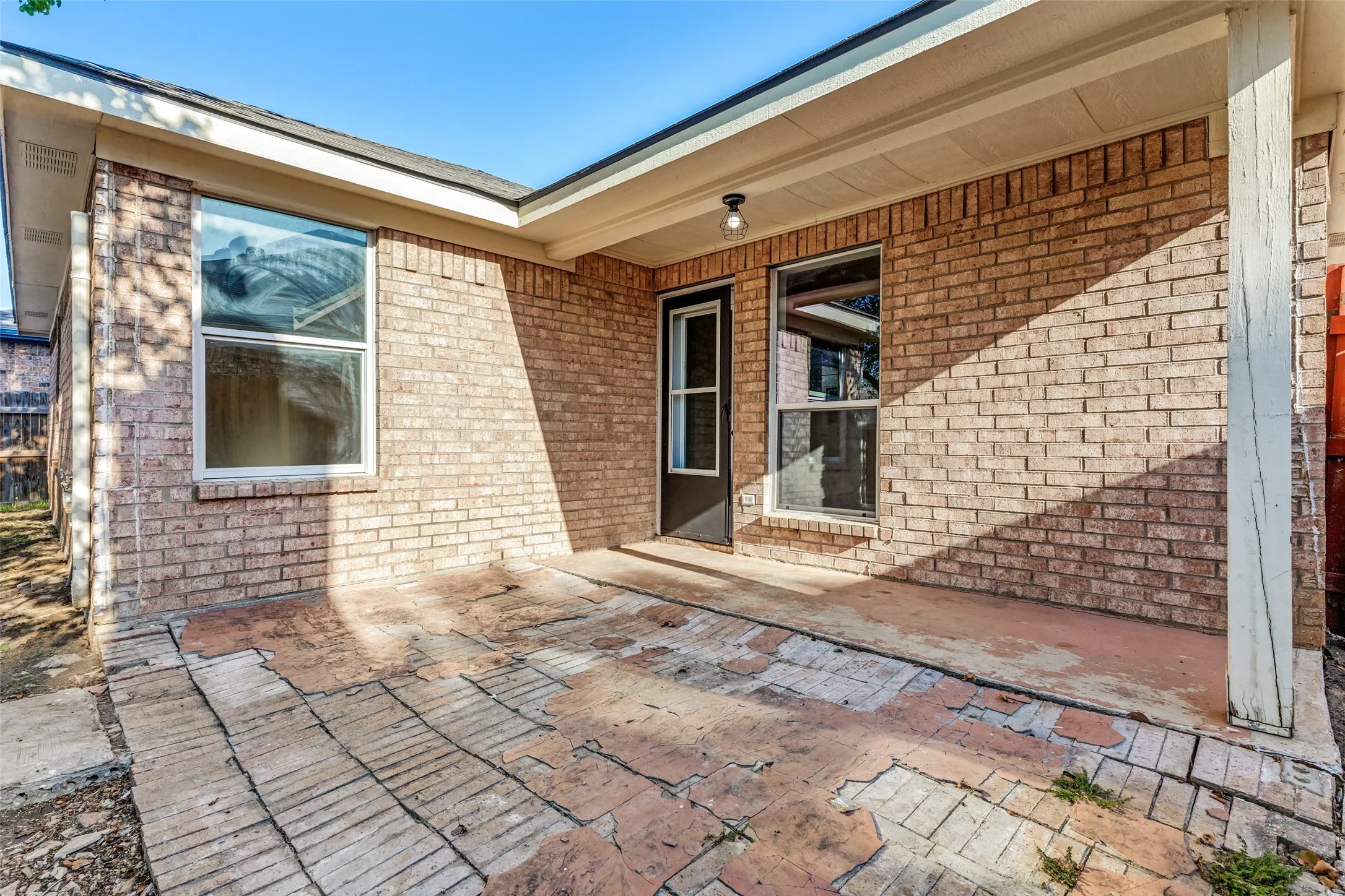 Covered patio with a brick veneer exterior, multiple windows, and exterior lighting