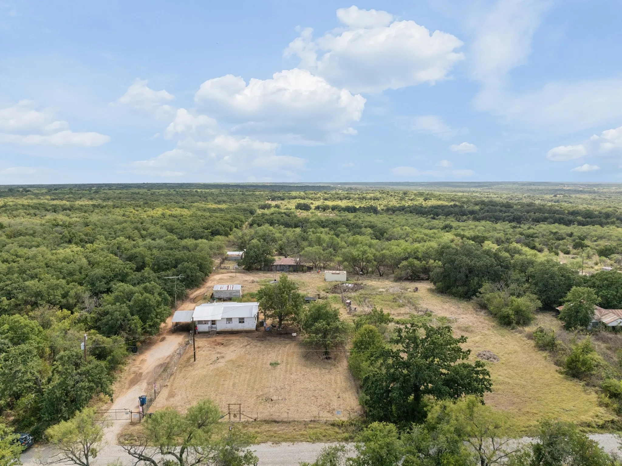 Expansive property featuring multiple structures, mature trees, and a gravel driveway