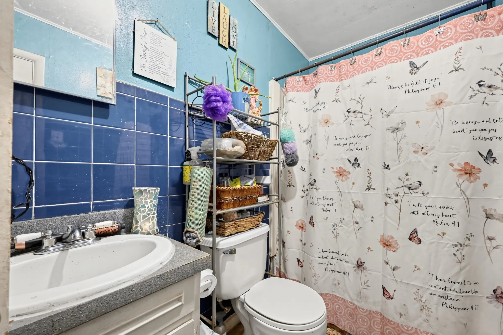 Bathroom featuring blue square wall tiling, a white oval sink with a dual-handle faucet, and a toilet