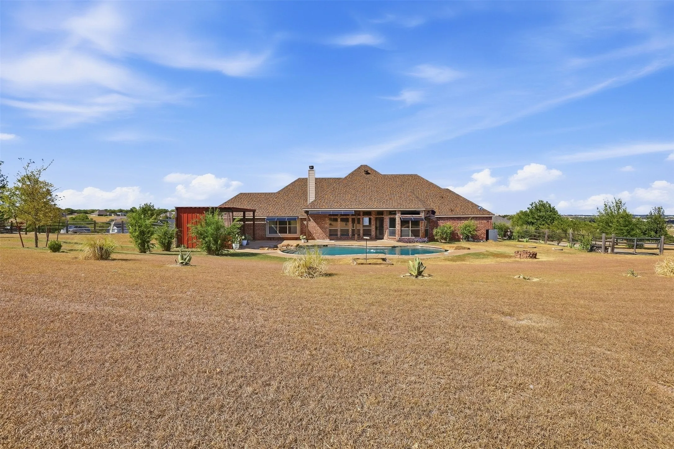 Brick exterior residence with an expansive backyard, featuring a swimming pool, covered patio, and attached pergola
