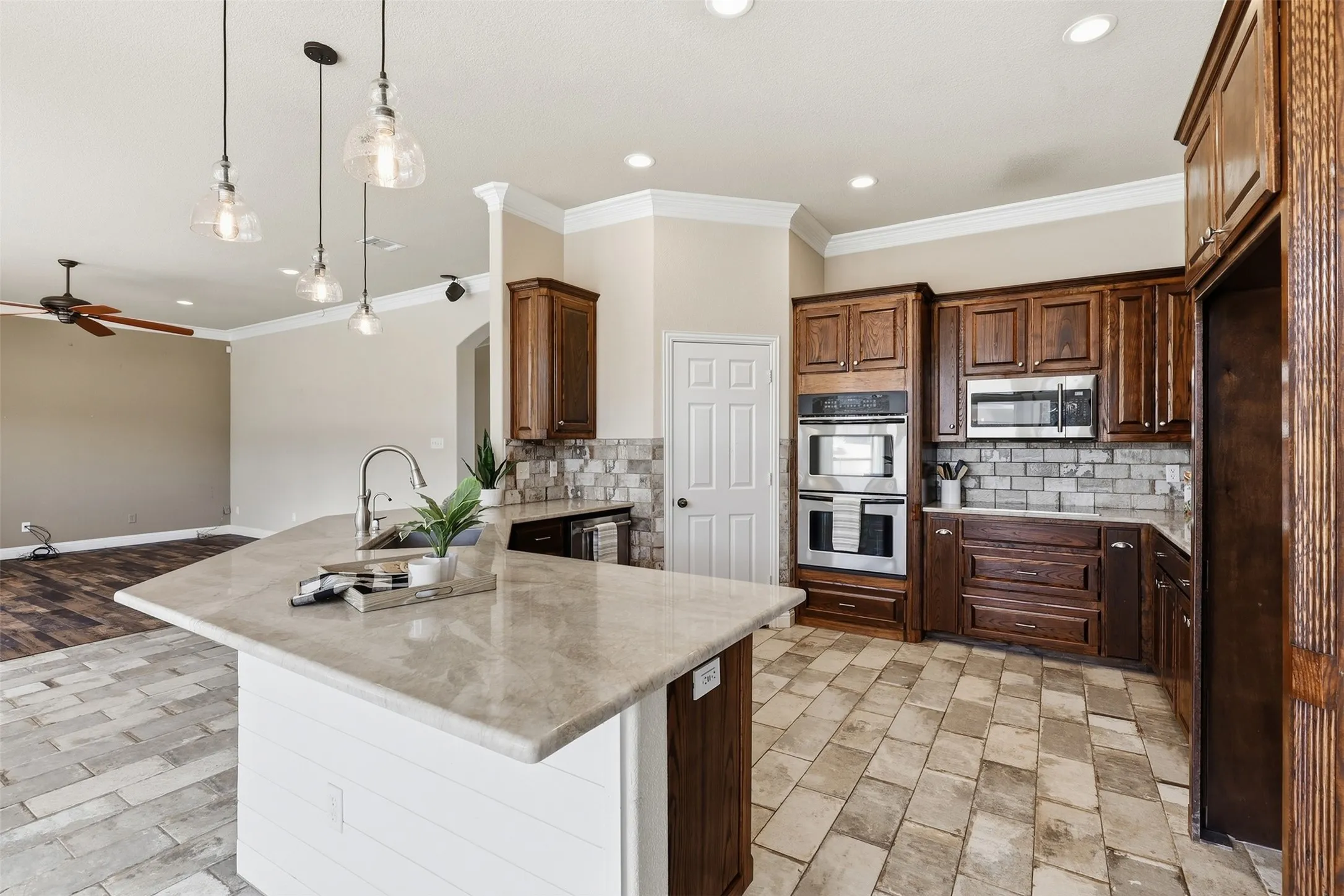 Kitchen featuring a central island with a sink, stainless steel appliances, dark wood-finish cabinetry, tile flooring, and a subway tile backsplash