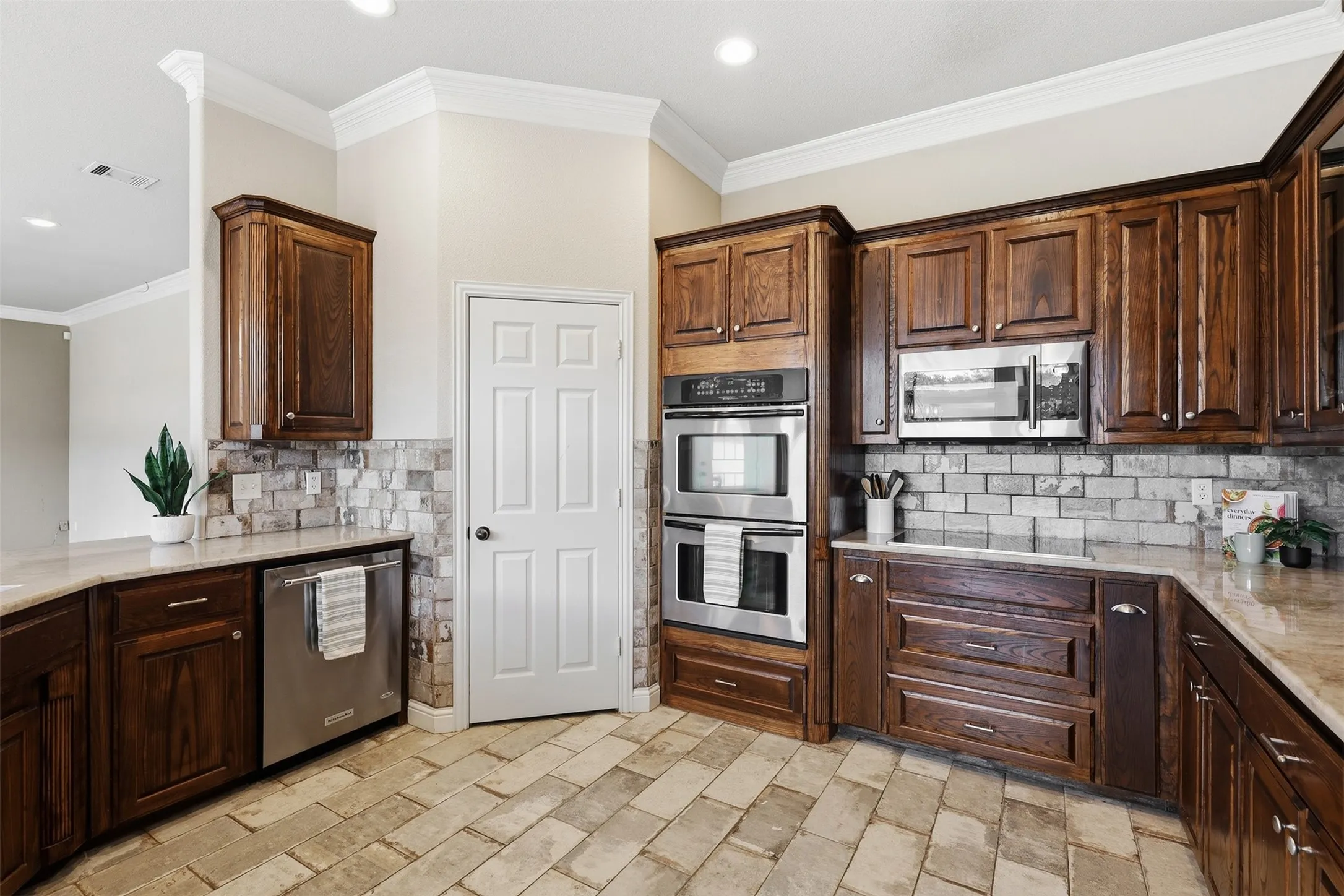 Kitchen featuring rich wood cabinetry, stainless steel appliances, stone countertops, a subway tile backsplash, and a decorative tile floor