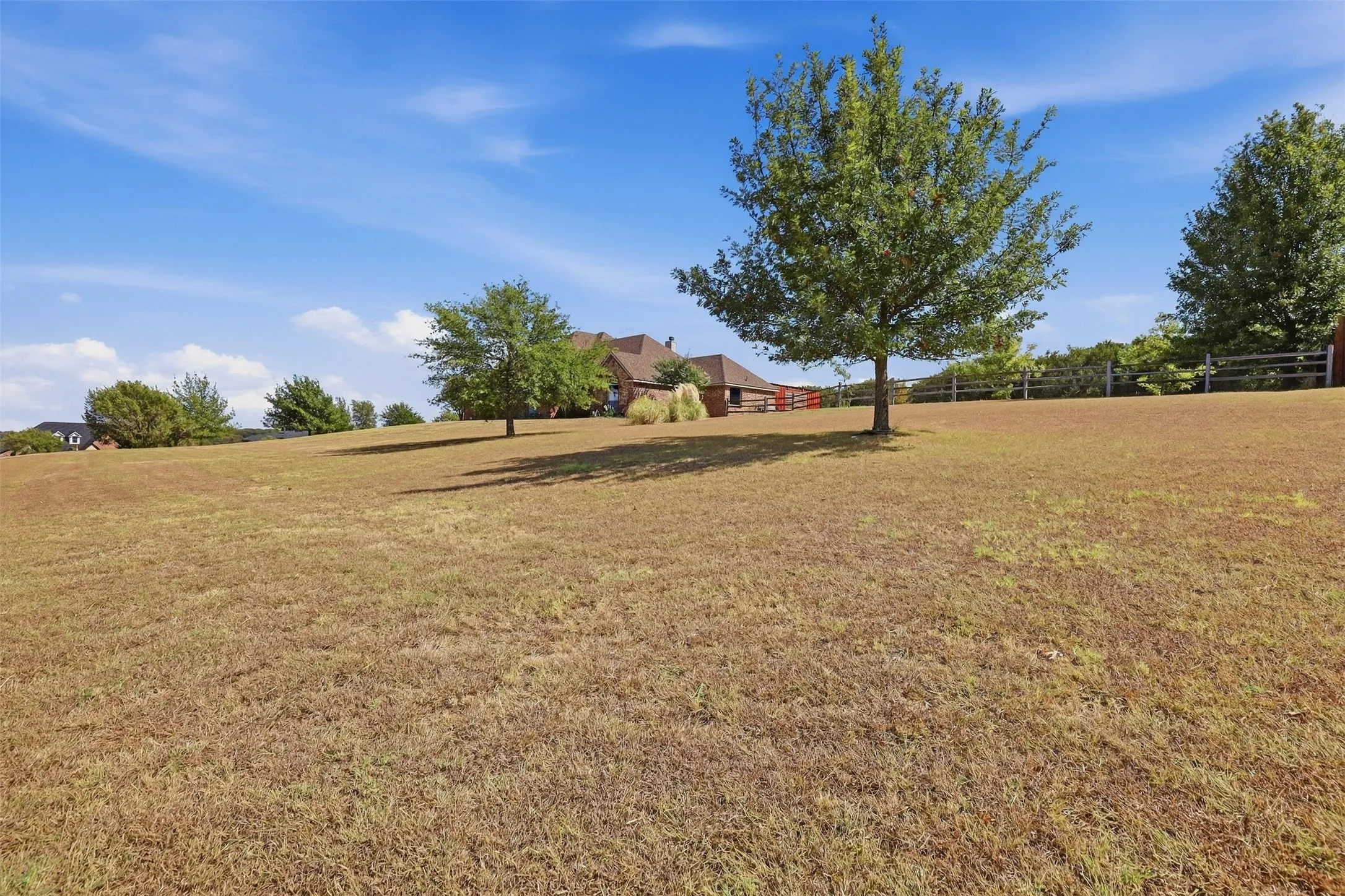 Expansive sloped lawn with scattered mature trees and a distant wood fence