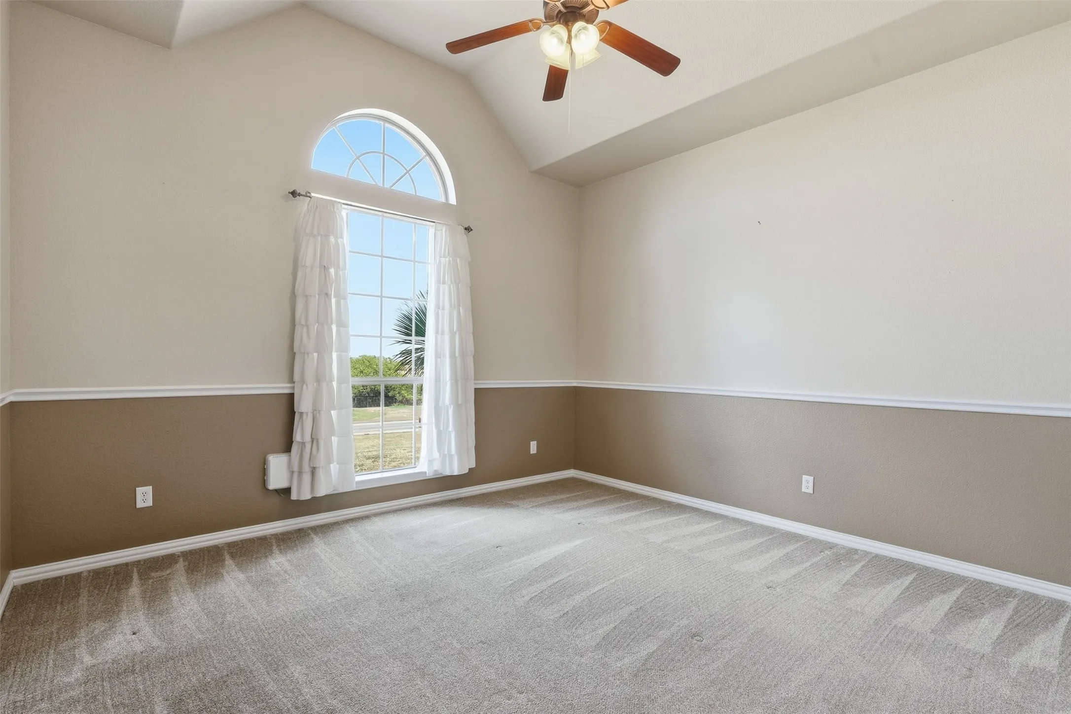 Vaulted ceiling with a ceiling fan, arched transom window, picture window, and chair rail molding