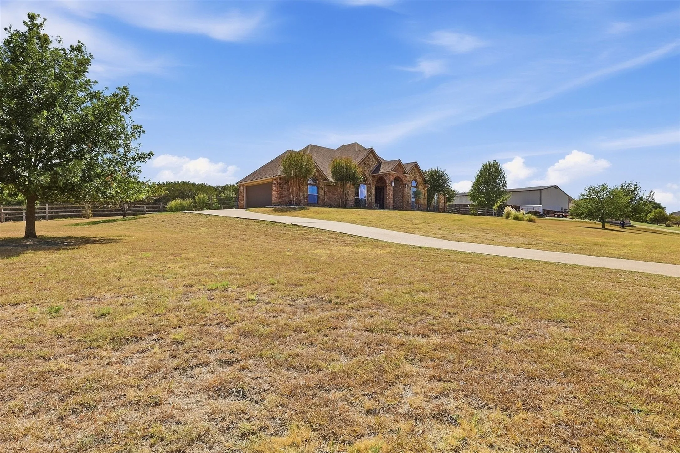 Brick exterior, gabled roofline, attached garage, concrete driveway, and a fenced perimeter