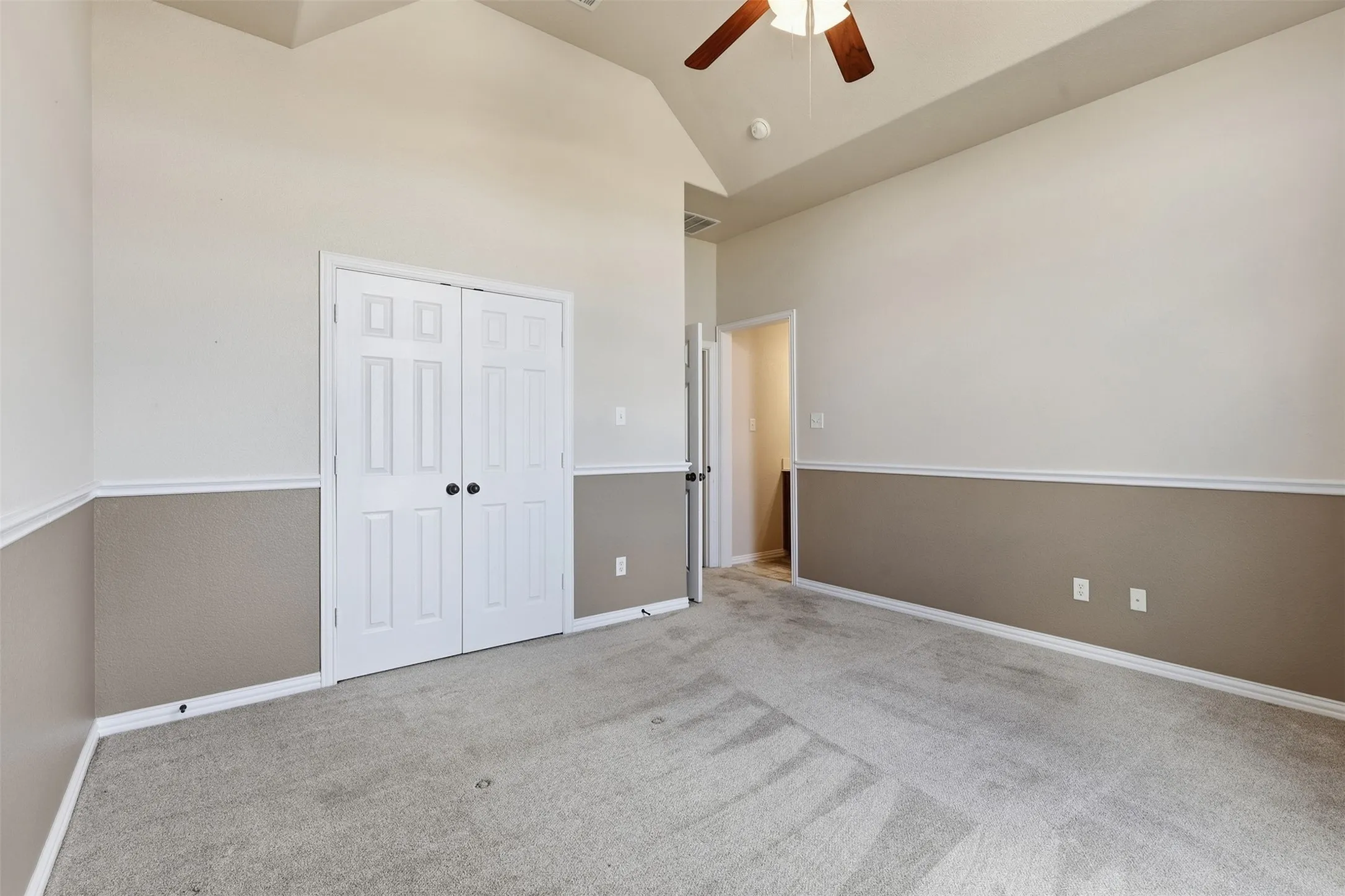 Vaulted ceiling, ceiling fan, bi-fold panel doors, two-tone wall treatment, and light-toned carpeting