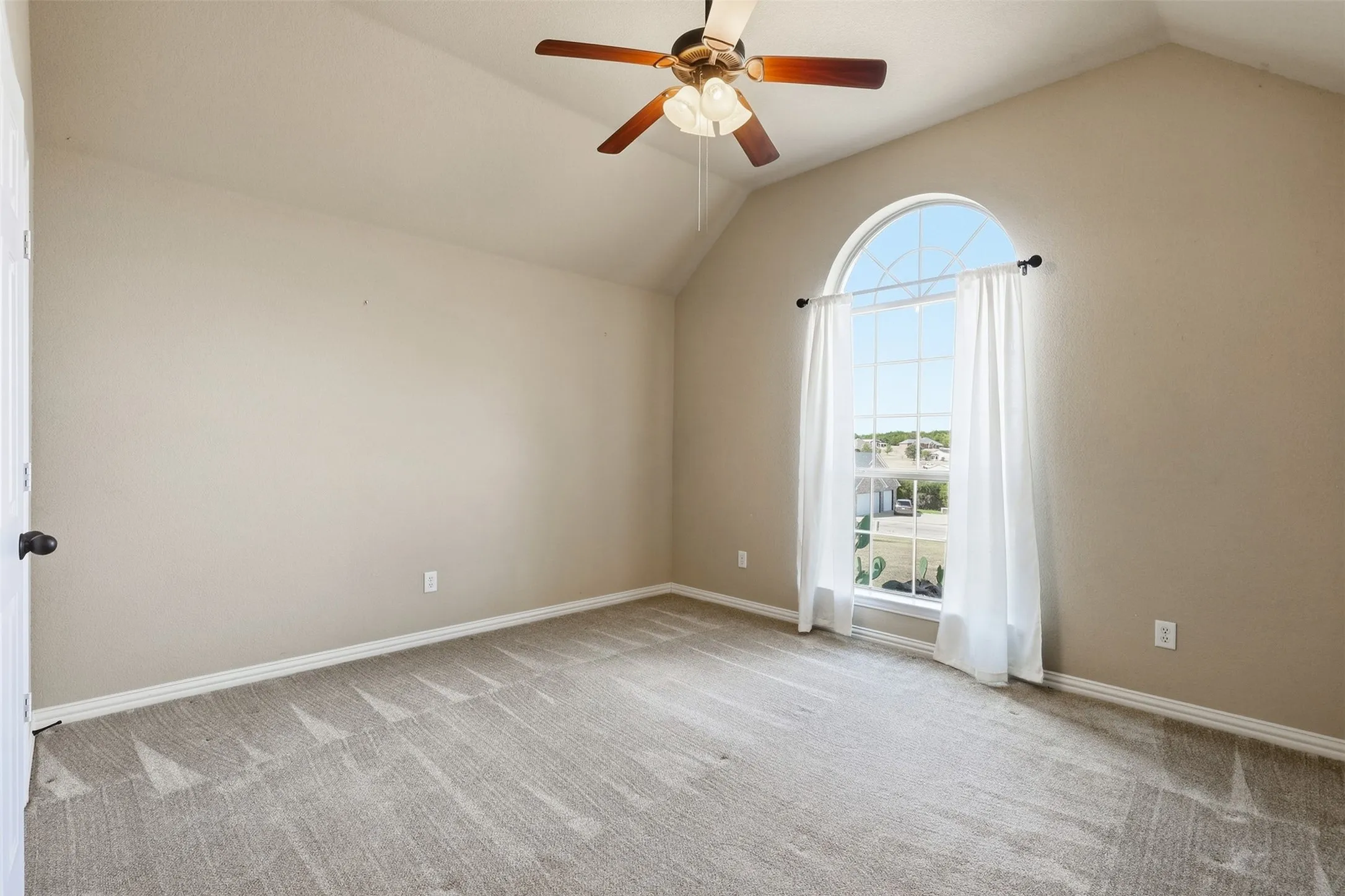 Vaulted ceiling, arched window, carpeted flooring, and a ceiling fan with light fixture