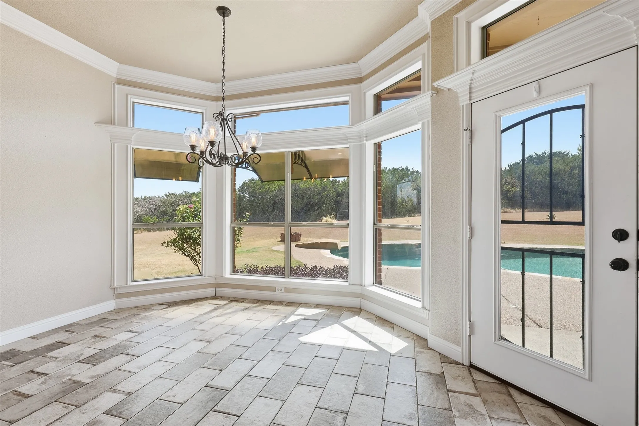 Bay window with multiple large panes, tile flooring, crown molding, and a decorative chandelier