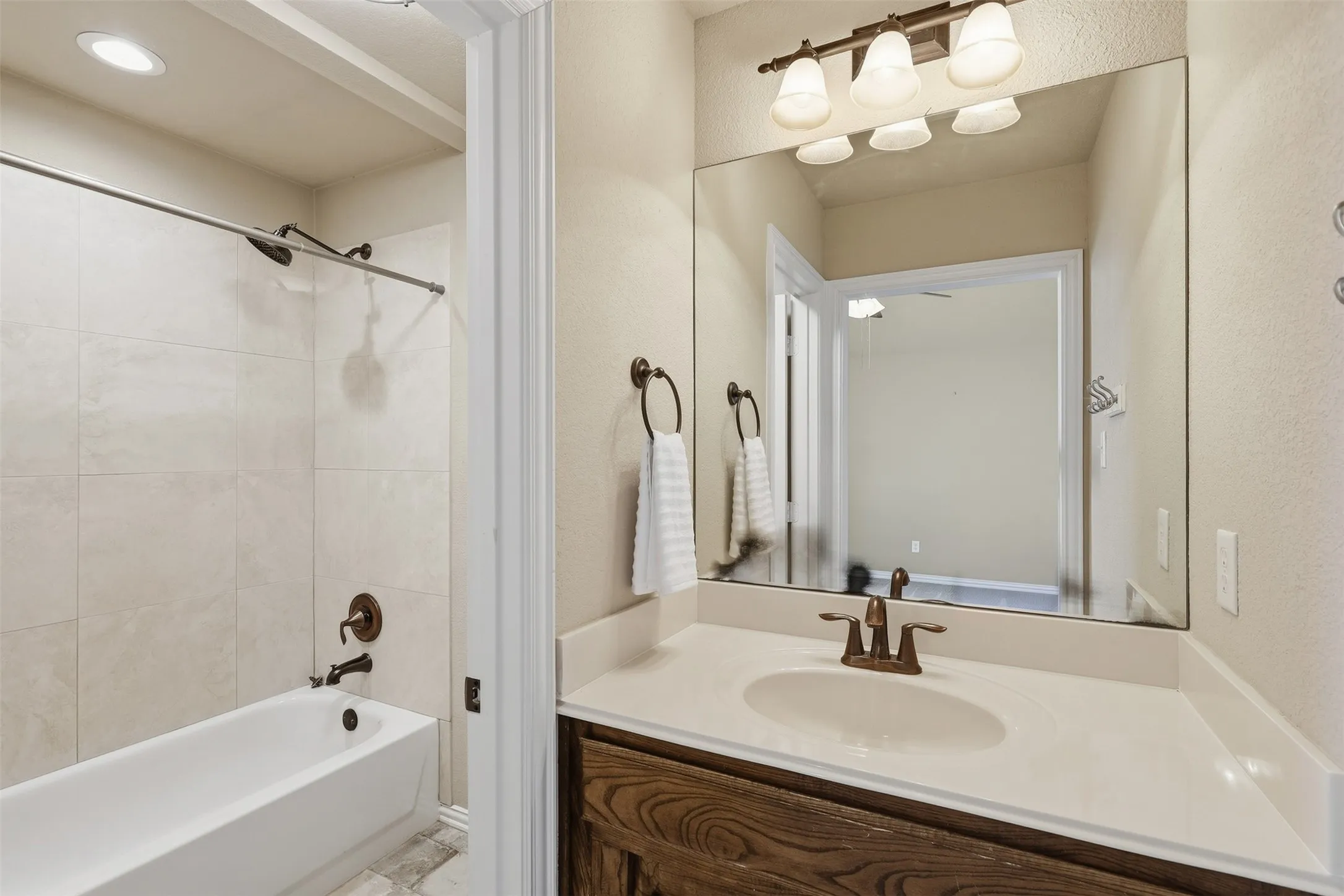 Full-size vanity mirror, single basin sink, bronze-finish faucet, and warm wood-finish cabinetry