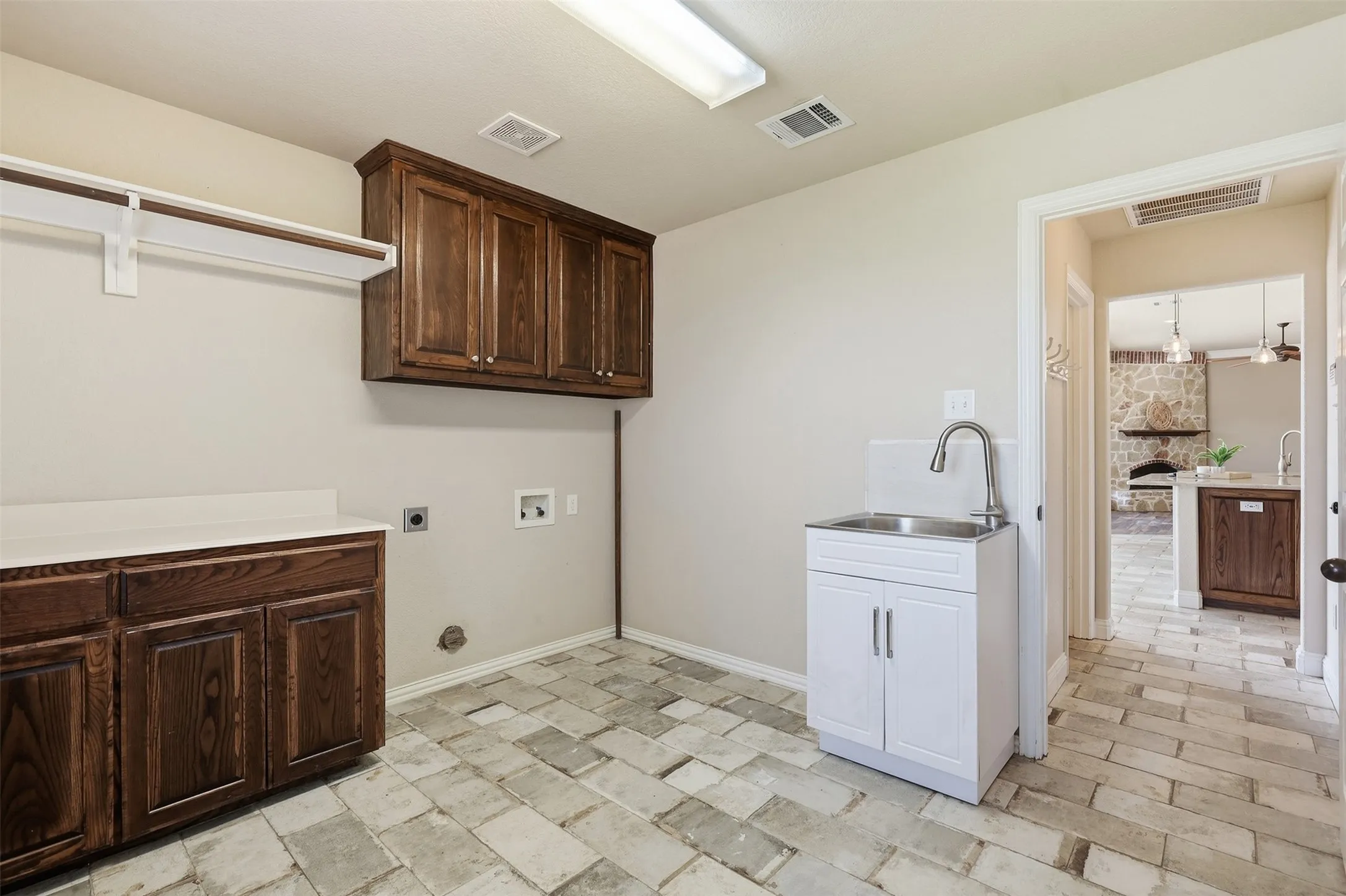 Built-in wood-finish cabinetry, white countertop, utility sink with chrome faucet, and rectangular floor tiles
