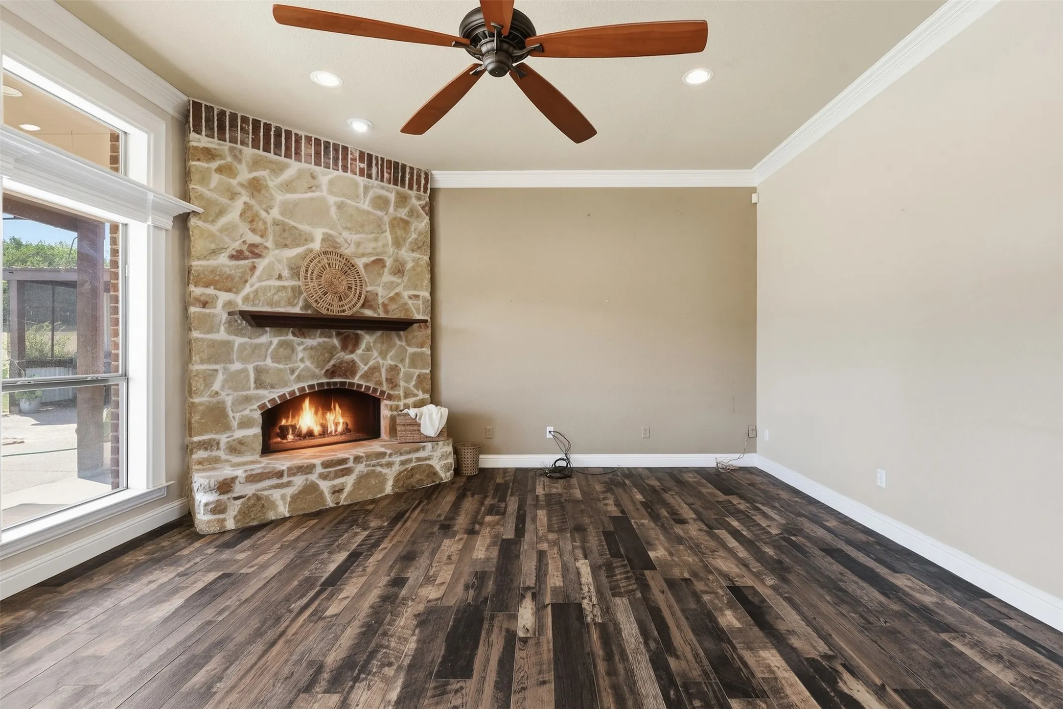 Corner stone fireplace with wood mantel, wood-finish flooring, recessed lighting, and a ceiling fan
