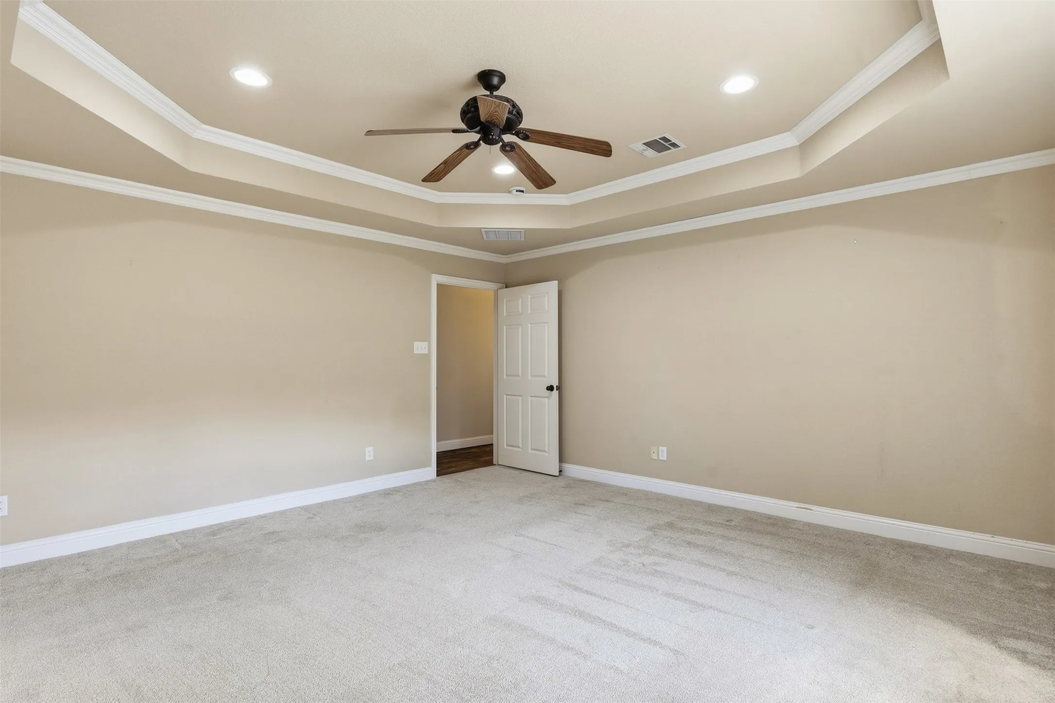 Tray ceiling with recessed lighting and a ceiling fan, light-colored carpet, and an interior door