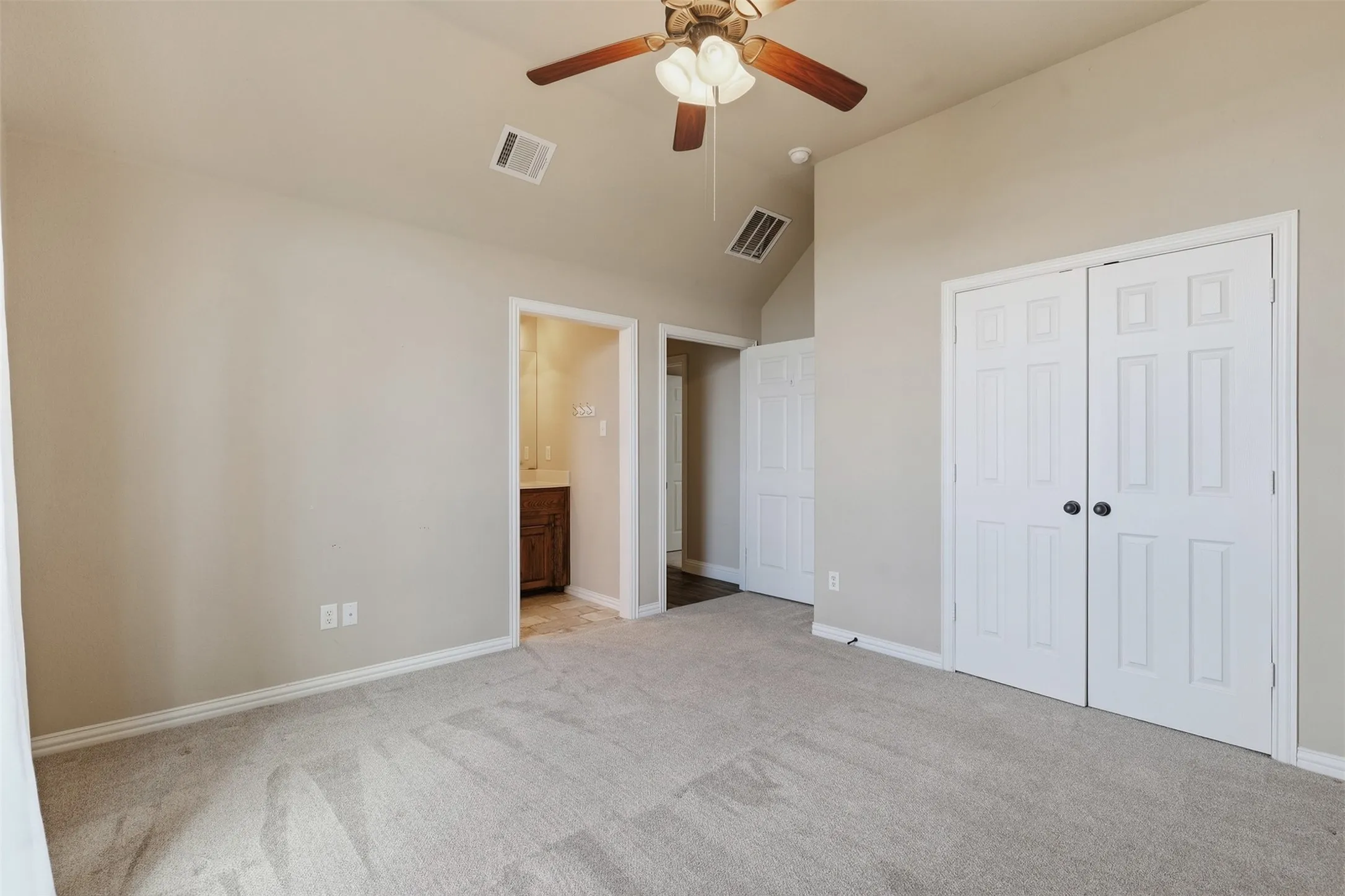 Vaulted ceiling with a ceiling fan, light gray carpeting, and paneled bifold closet doors