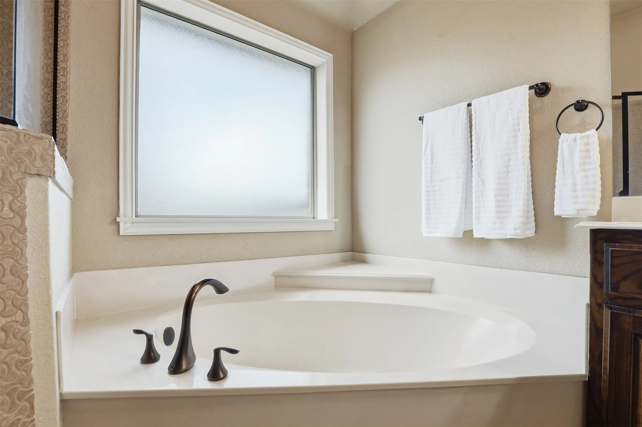 Built-in soaking tub with bronze-finish fixtures, a frosted window, and a surrounding light-toned countertop