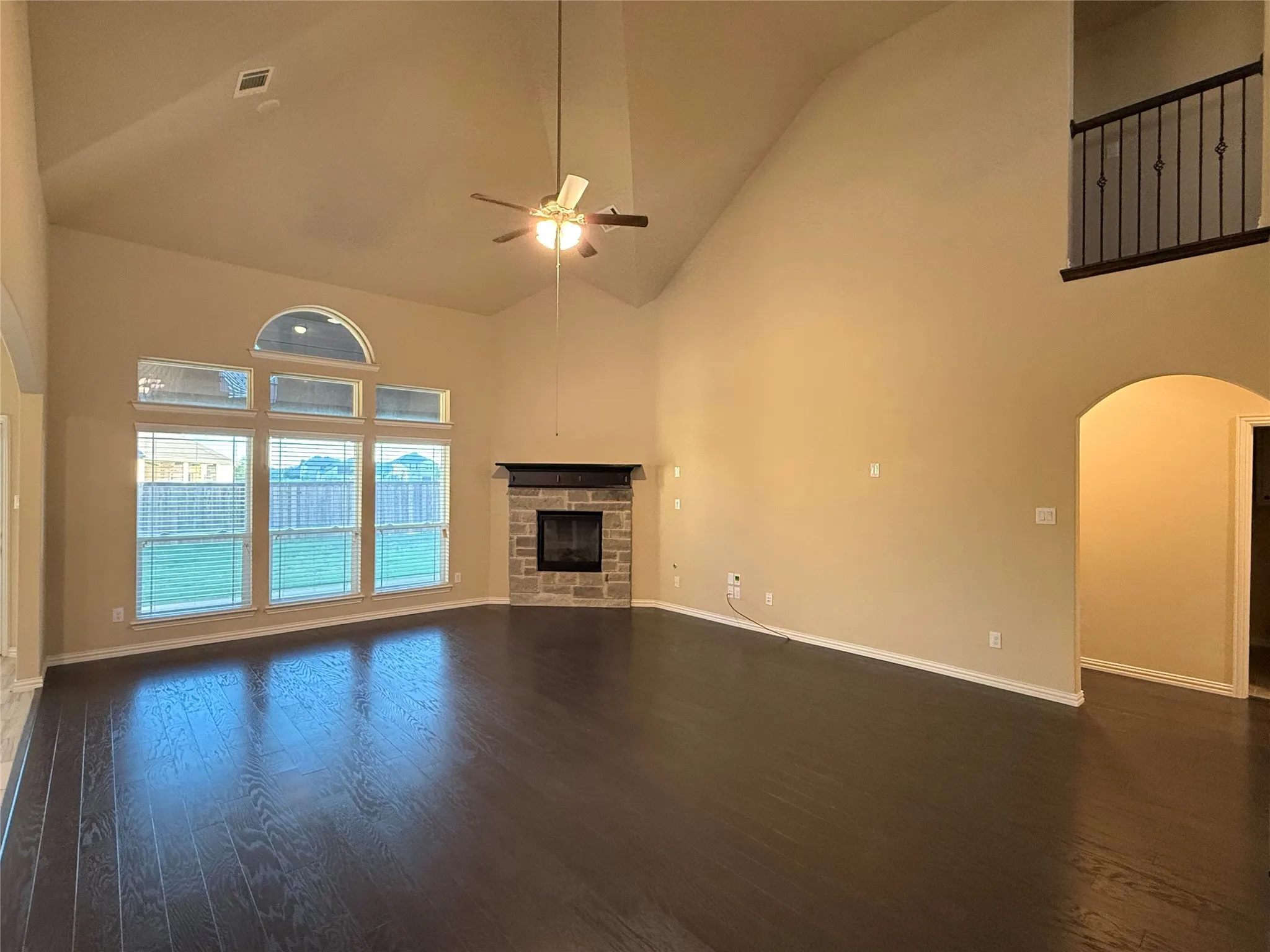 Vaulted ceiling, wood-finish flooring, stone-clad fireplace, arched doorway, and expansive windows