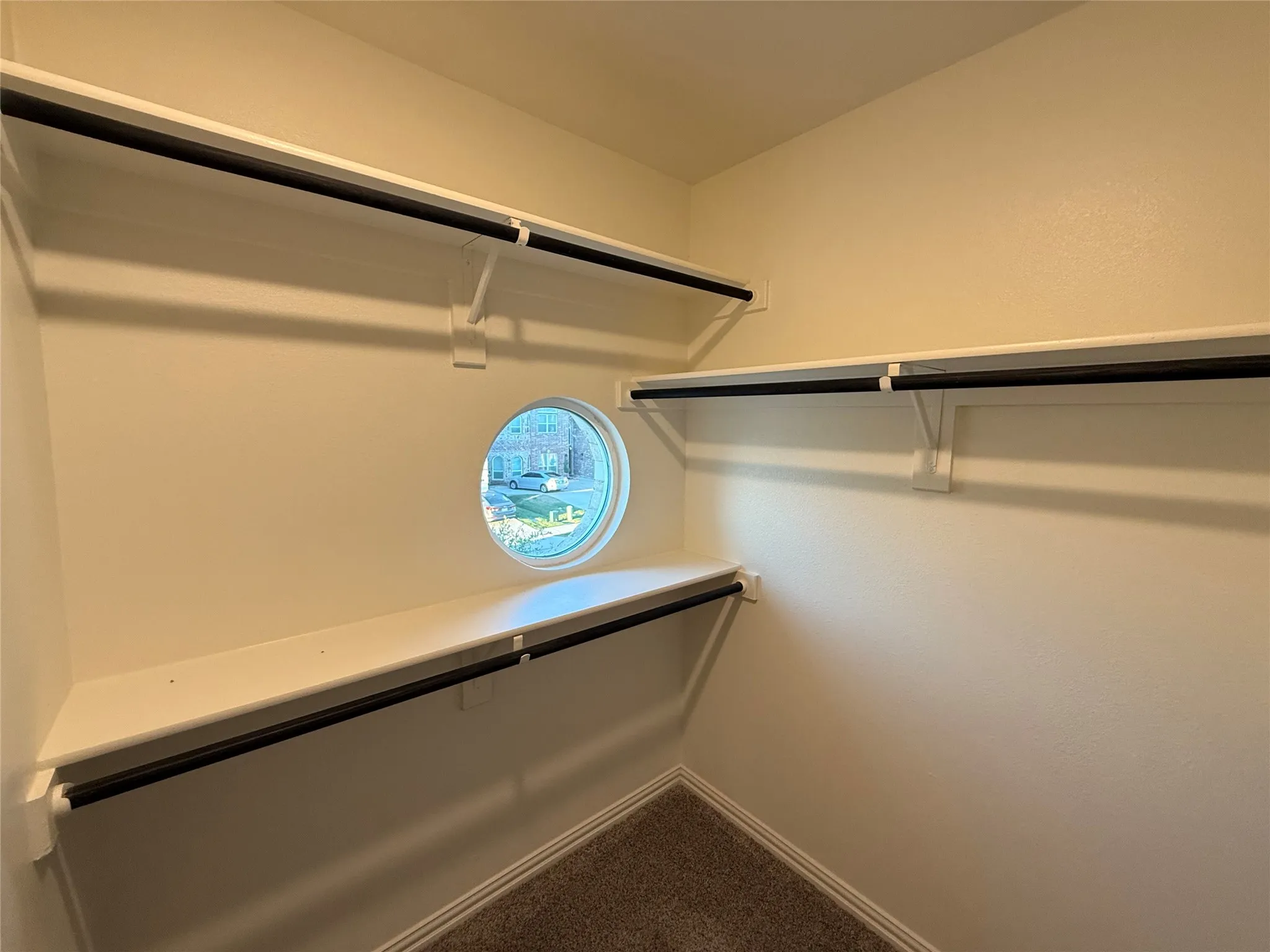 Built-in shelving with hanging rods, circular window, and carpet flooring