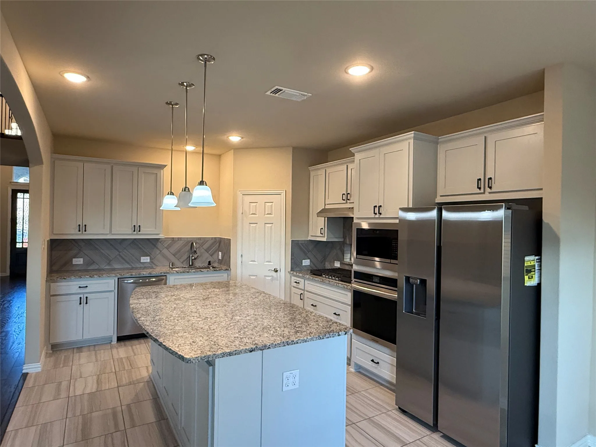 Kitchen featuring a central island with a stone countertop, stainless steel appliances, light-toned cabinetry, a tiled backsplash, and recessed lighting
