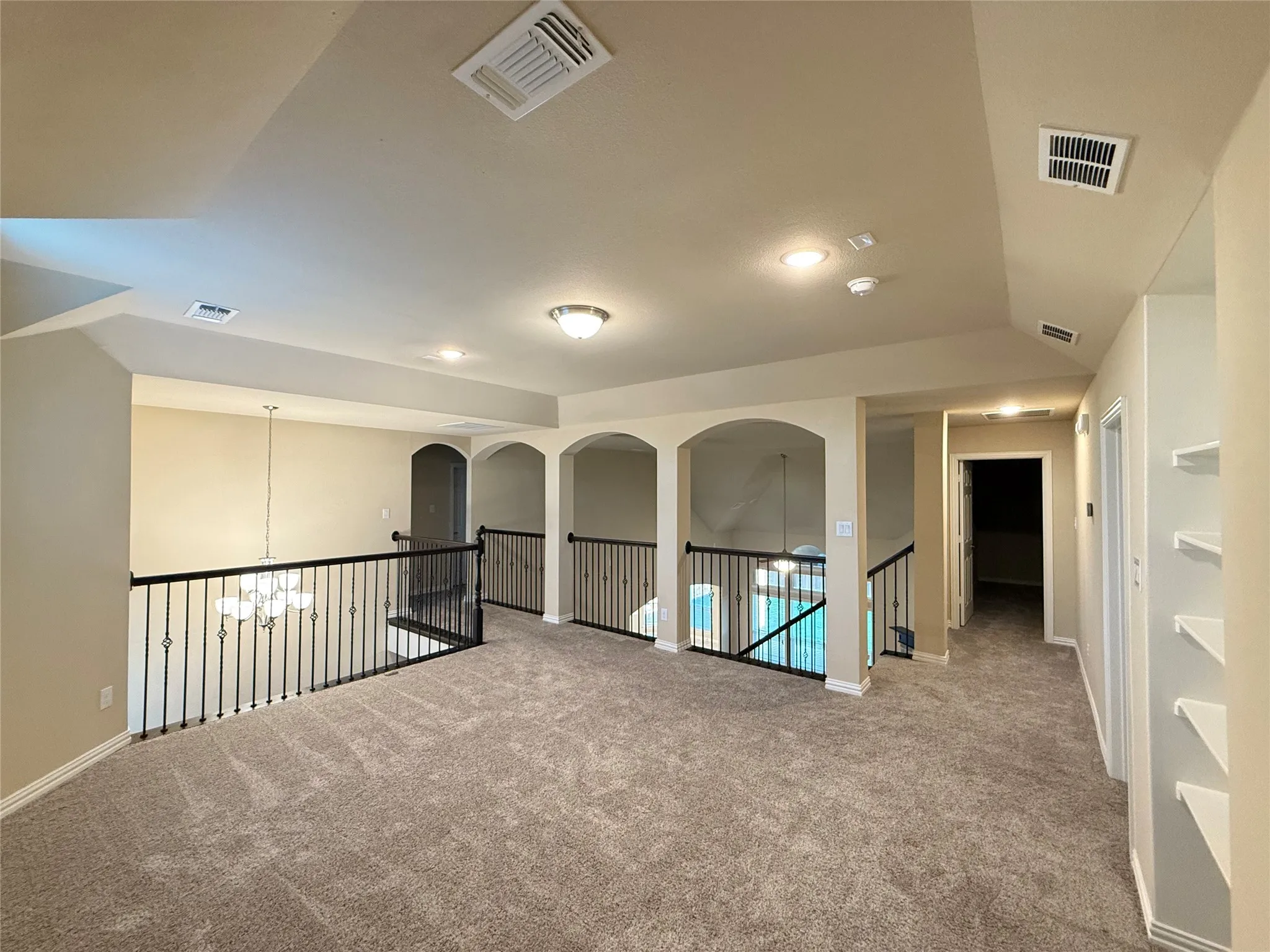 Expansive carpeted loft area with wrought iron railings, arched openings, recessed lighting, and built-in shelving