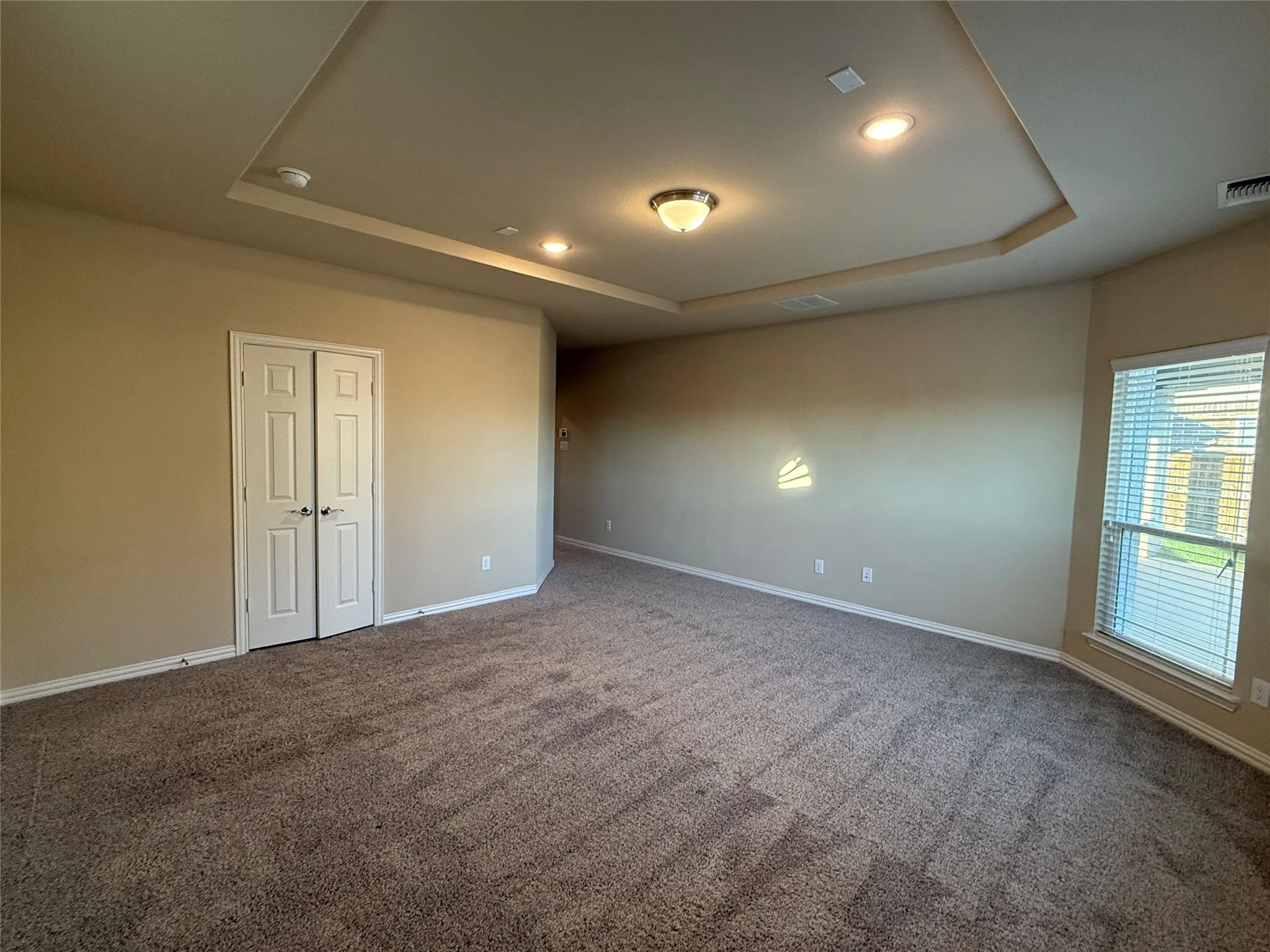 Tray ceiling with recessed lighting and a central flush-mount fixture, neutral carpet flooring, and a window with blinds