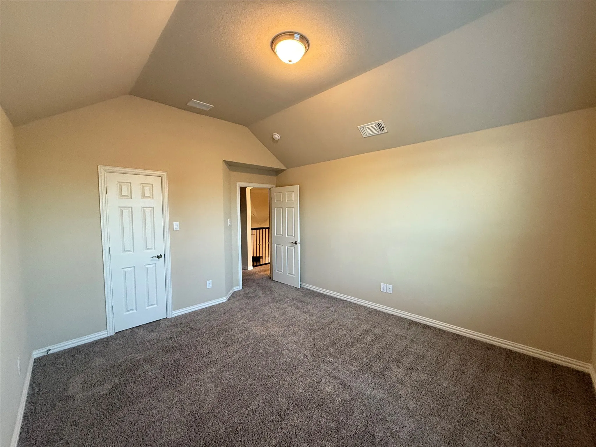 Neutral-toned walls with vaulted ceiling, plush carpet flooring, and a flush-mount ceiling light fixture