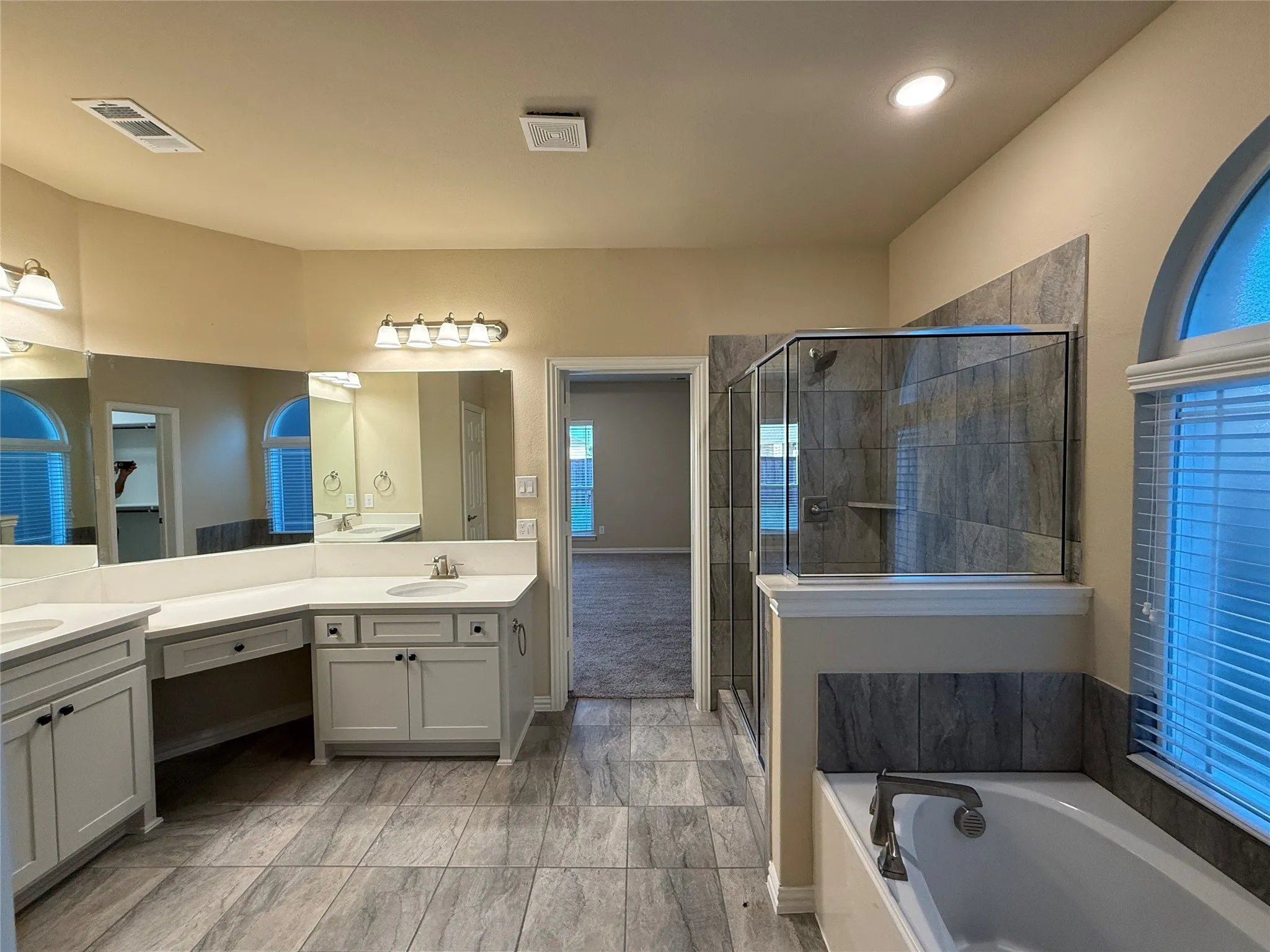 Bathroom featuring dual vanities with white countertops, a built-in shower with glass enclosure, a separate bathtub, and tile flooring