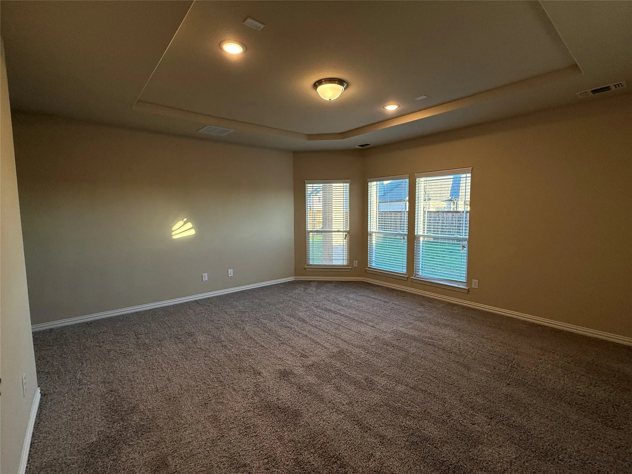 Tray ceiling with recessed lighting, integrated ceiling light fixture, three windows with blinds, wall-to-wall carpeting, and neutral wall tones
