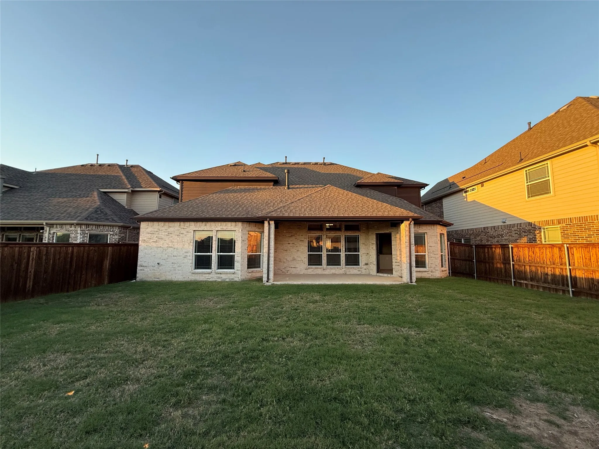 Expansive backyard featuring a manicured lawn, full privacy fencing, and a covered patio with recessed lighting
