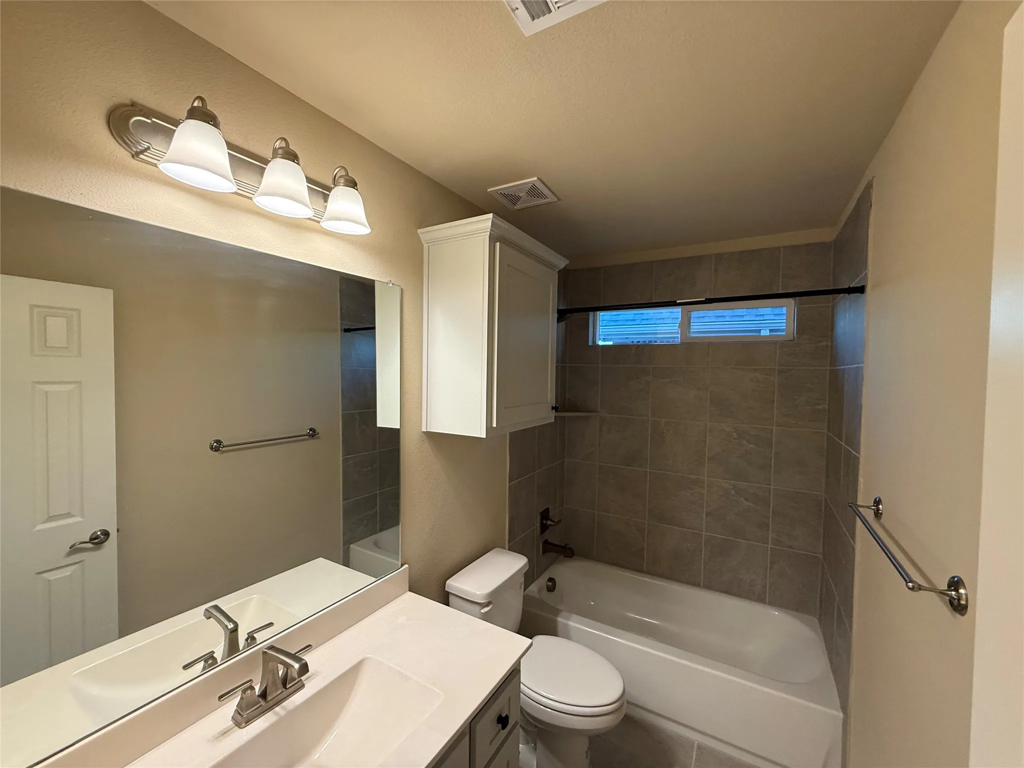 Vanity with a rectangular sink and brushed nickel faucet, large mirror, wall-mounted storage cabinet, tiled shower surround, and a built-in tub