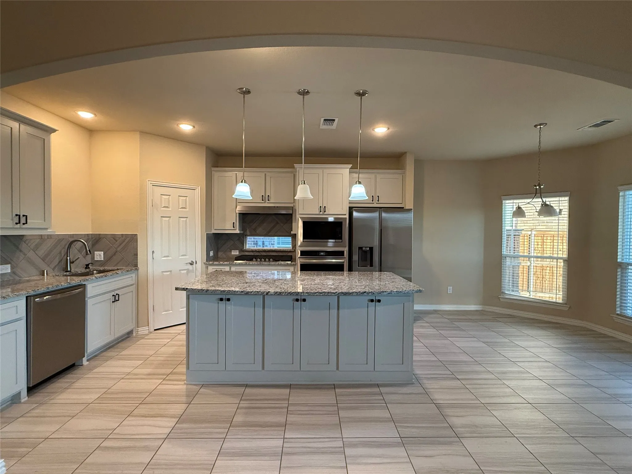 Kitchen featuring an arched entryway, light-toned cabinetry, a center island with pendant lighting, stone countertops, and tile flooring