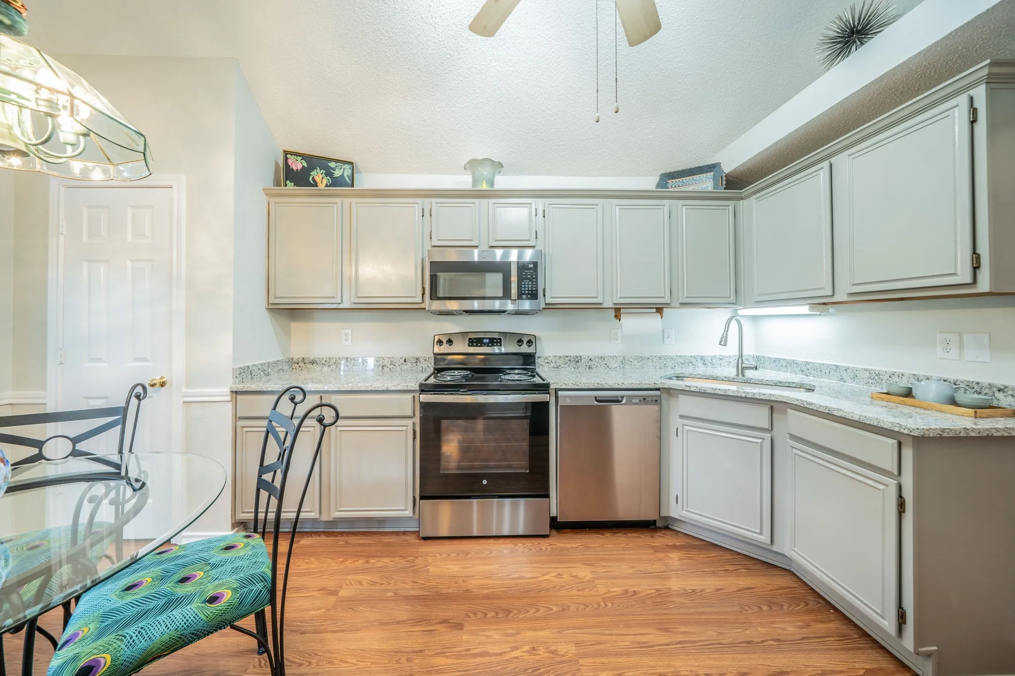 Kitchen featuring wood-finish flooring, granite countertops, stainless steel appliances, and light-toned cabinetry with under-cabinet lighting, new granite and ss appliances, sink and disposal
