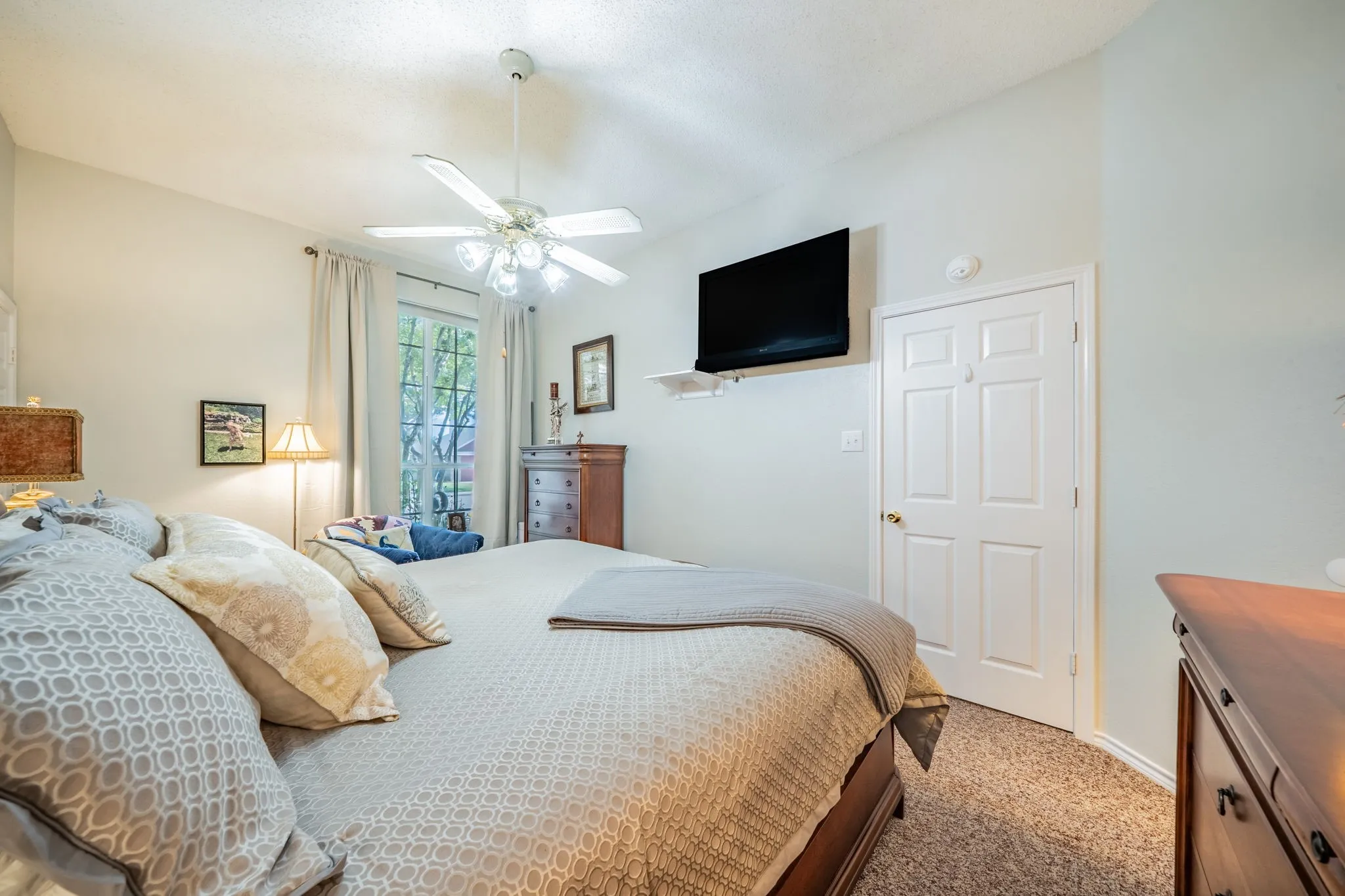 Recessed window with white curtains, ceiling fan with light fixture, carpeted flooring, white paneled door