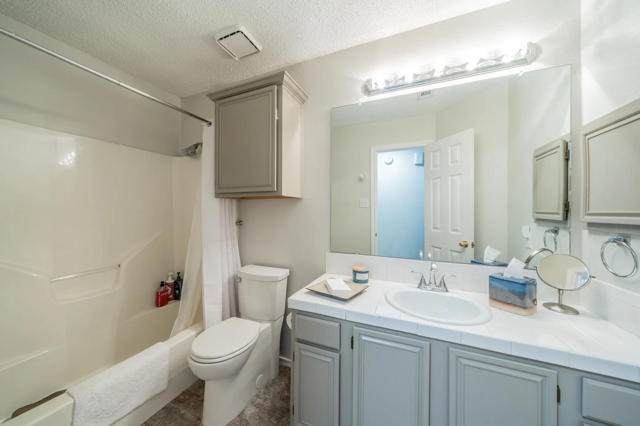 Full vanity with a single basin sink, wall-mounted mirror, and overhead lighting