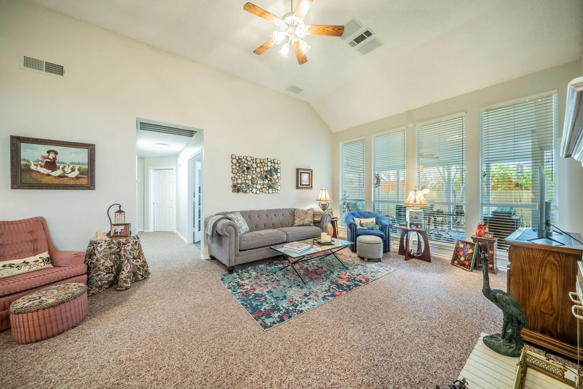 Vaulted ceiling with a ceiling fan, light-colored walls, spacious and  large expansive windows.
