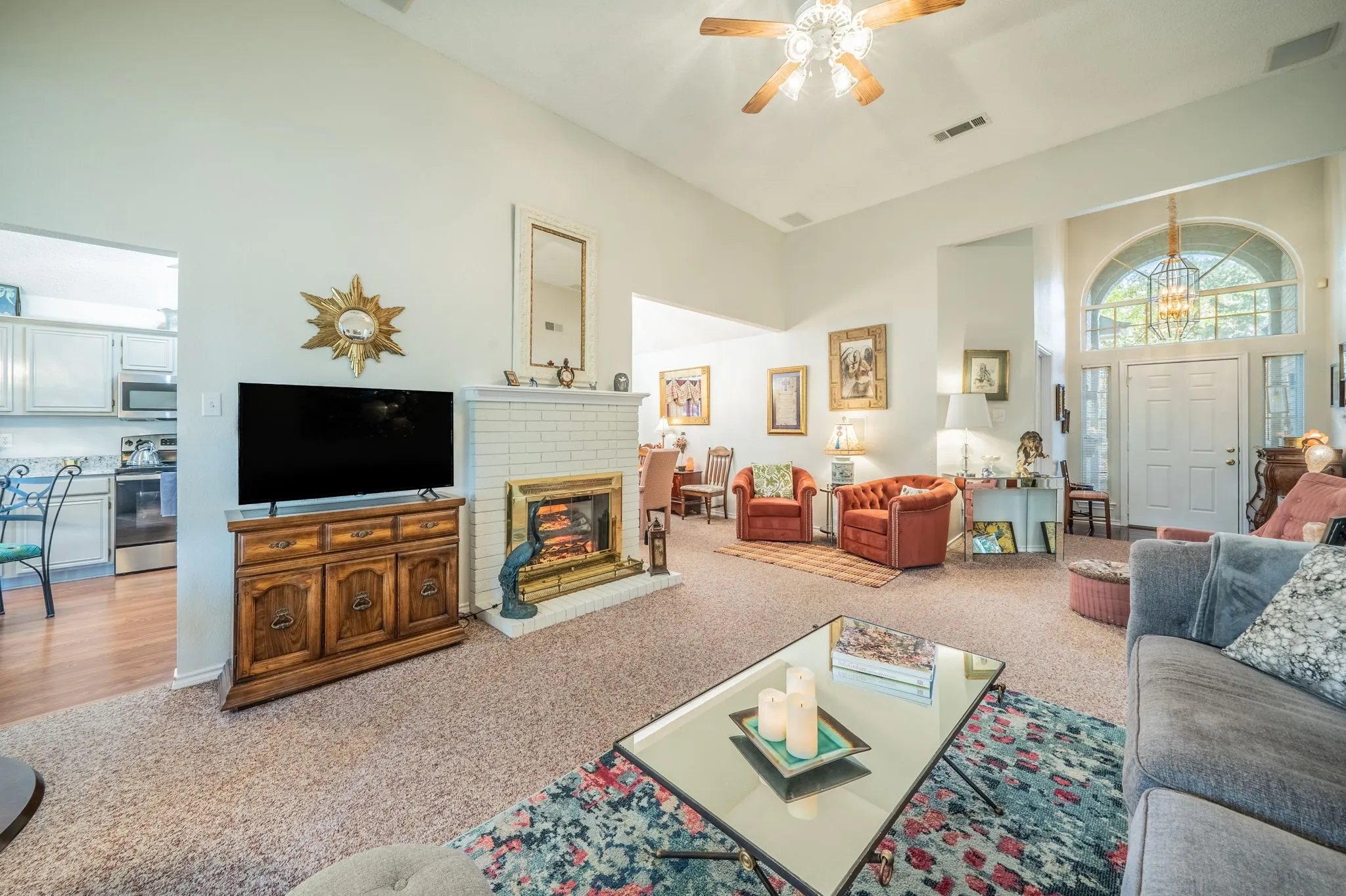 Vaulted ceilings with a ceiling fan, a white brick fireplace with a brass-tone insert, a white entry door with an arched transom window. complete professional interior paint 2026