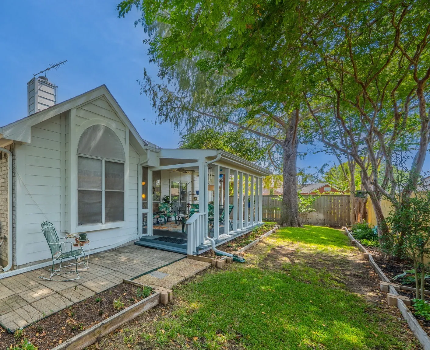 Paved area for grill or additional seating. featuring a manicured lawn, established trees, and a wooden privacy fence