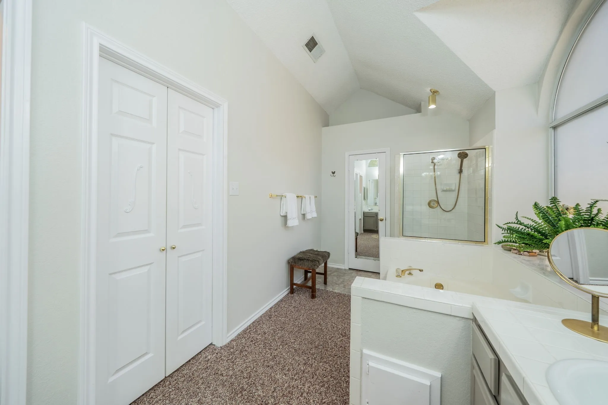 Vaulted ceiling, arched window, built-in jetted bathtub, glass-enclosed shower, and bi-fold doors