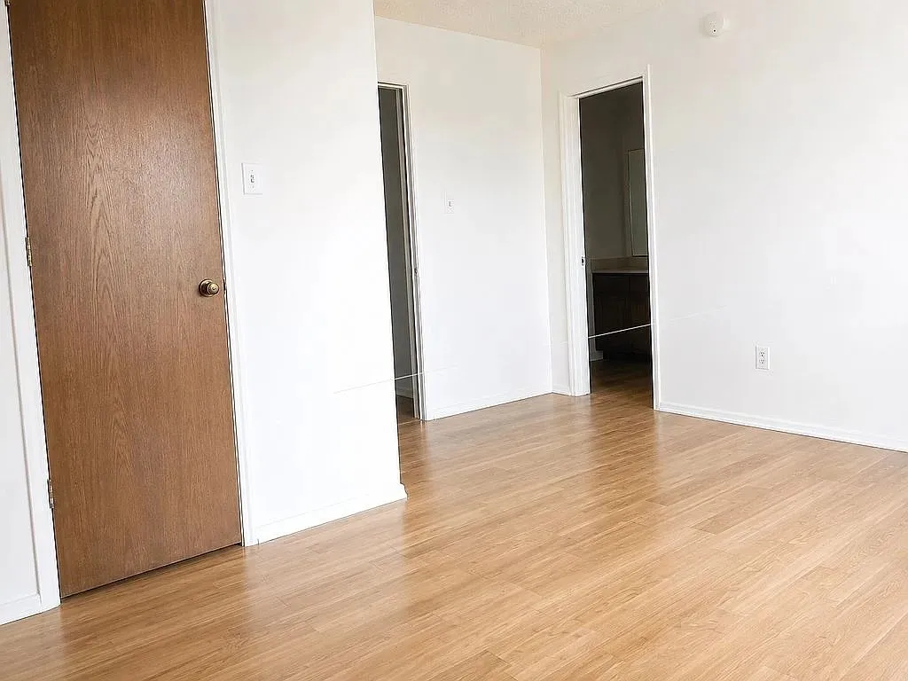 Wood-finish flooring throughout, white walls, and a recessed doorway leading to an additional space