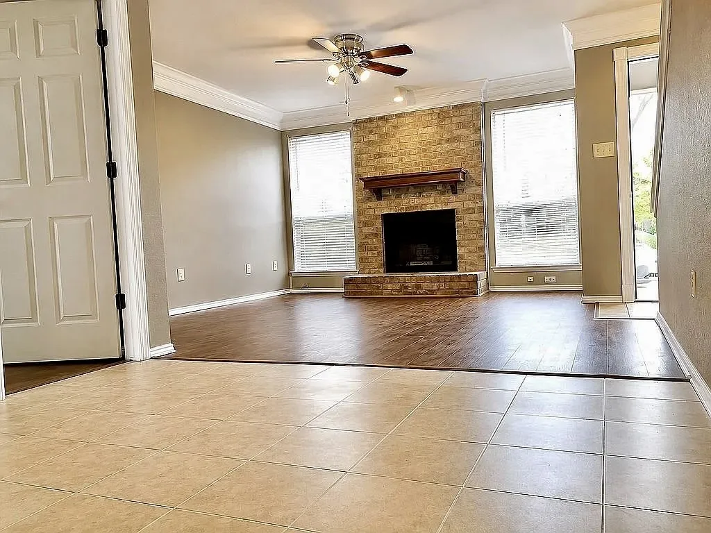Living area with wood-finish flooring, a brick-surround fireplace with a wood mantle, and crown molding