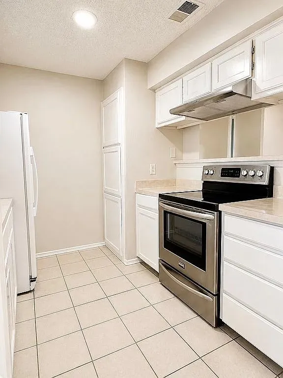 White paneled cabinetry, stainless steel range with overhead ventilation, light-toned countertop, and recessed ceiling lighting