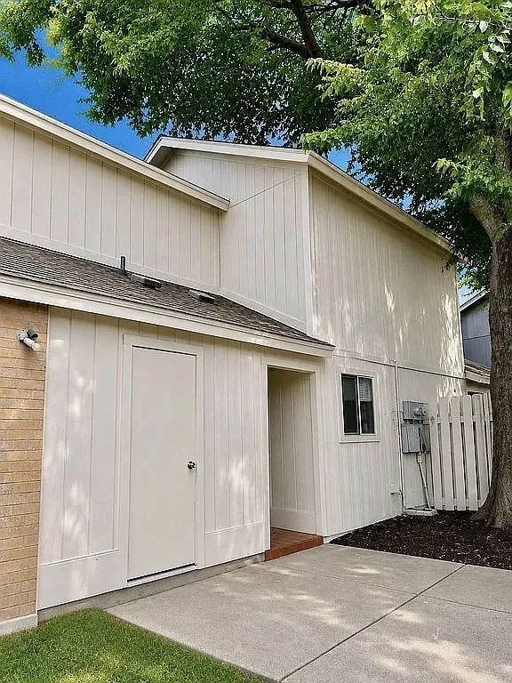 Exterior featuring board and batten siding, brick facade, shingled roofing, concrete patio, and a wood privacy fence