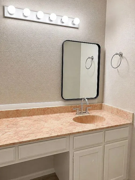 Vanity featuring a stone-look countertop, integrated sink, chrome faucet, and white cabinetry